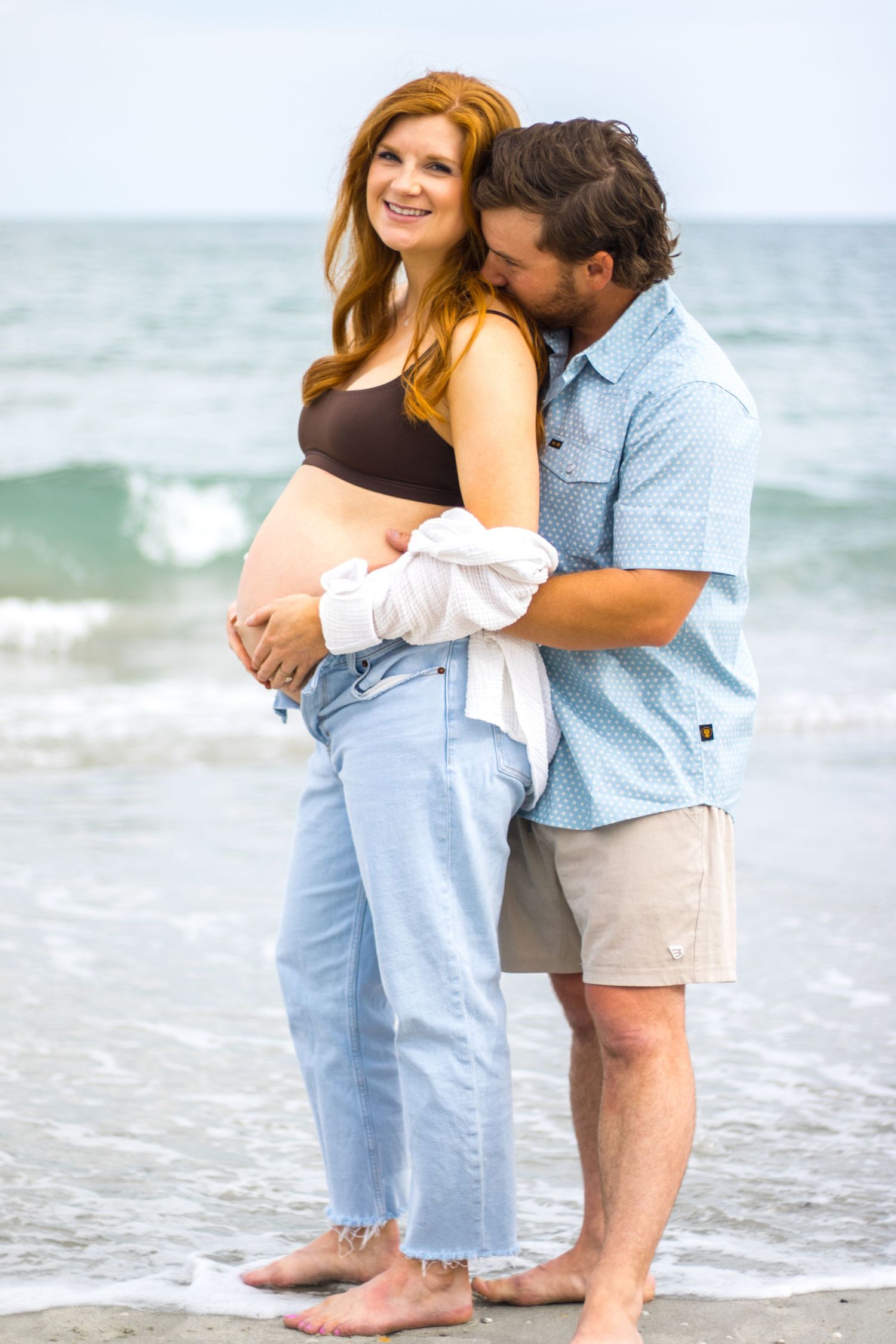 An intimate beachside moment captured with ocean waves in the background.