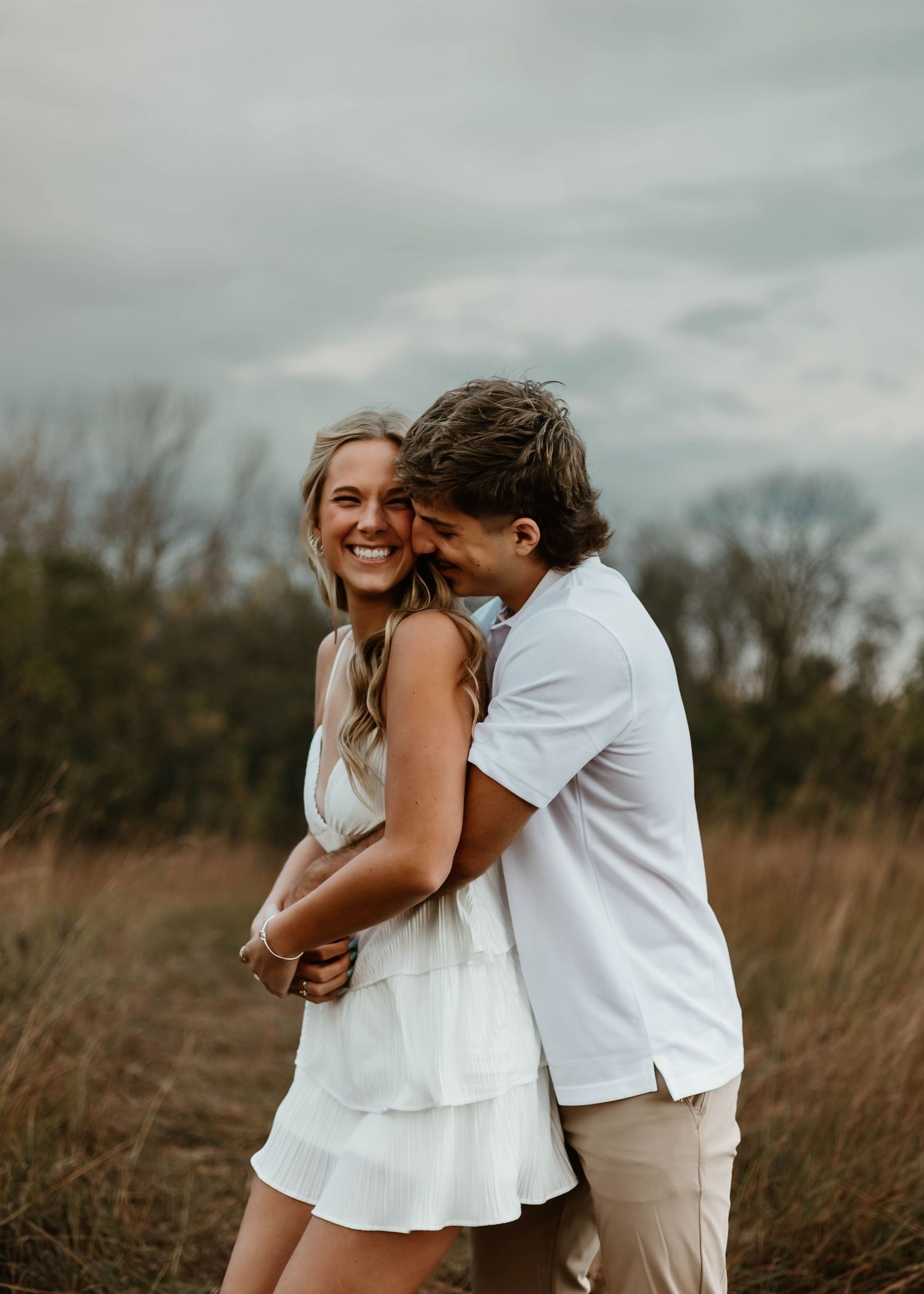 An intimate embrace between a couple wearing white and khaki in a natural outdoor setting.