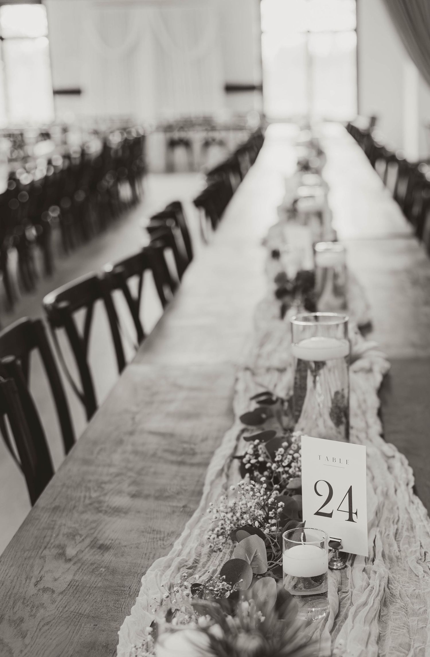 Long rustic wedding reception tables with table numbers and place settings in black and white.