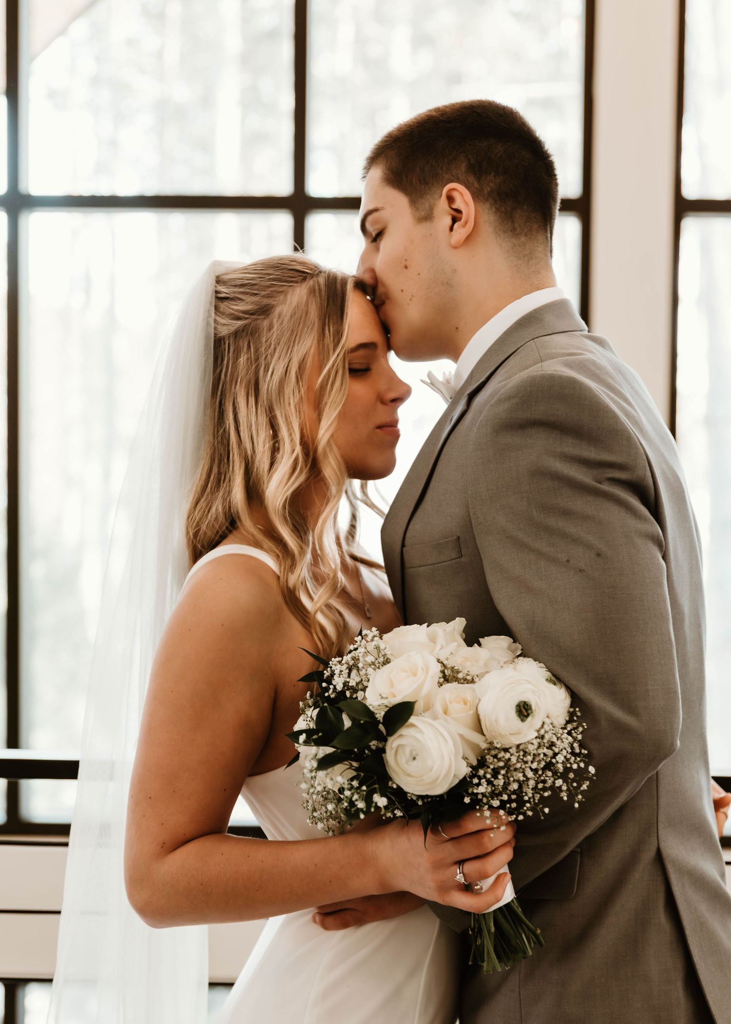 A romantic winter wedding moment captured through window panes with white flowers.