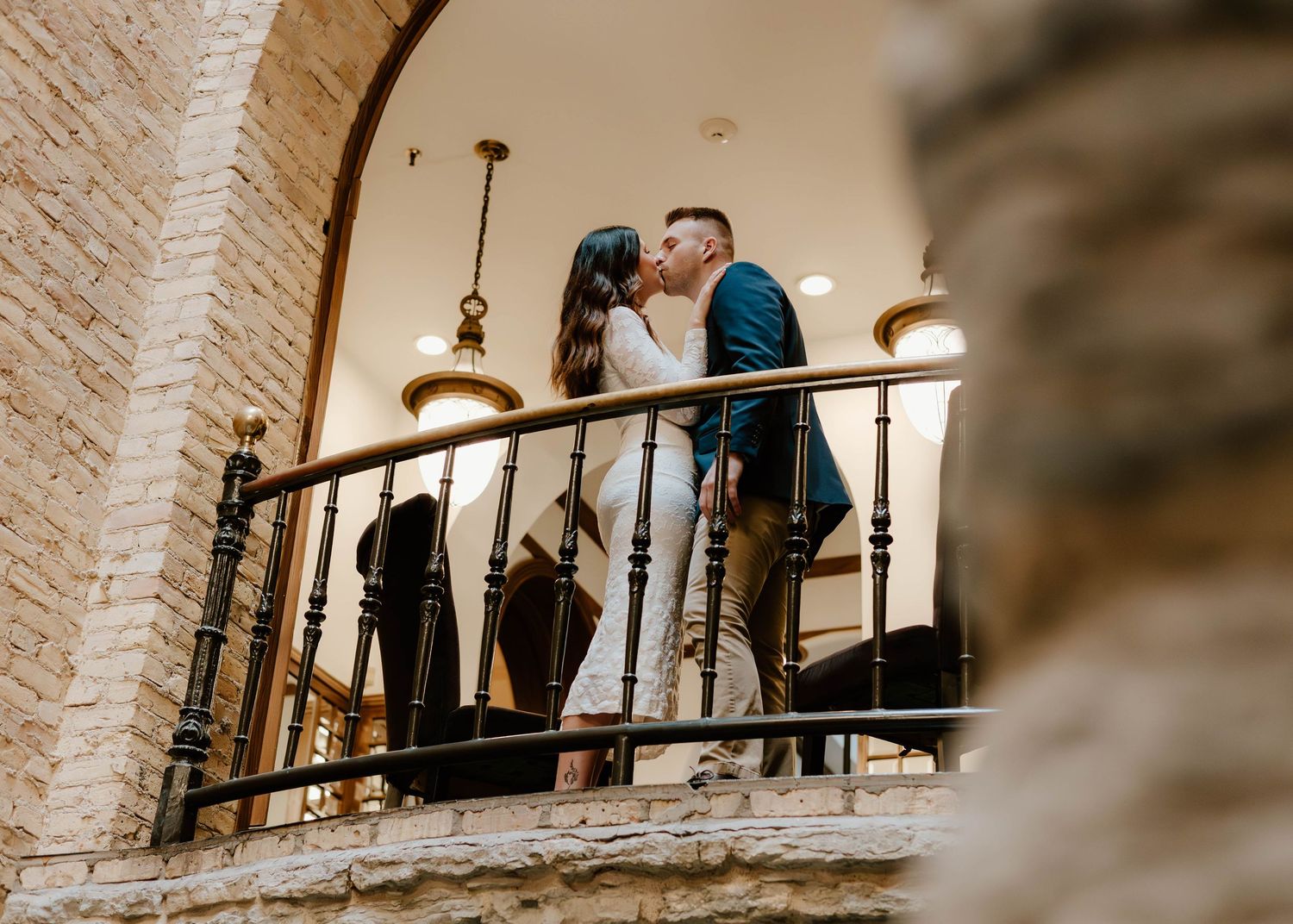 A romantic moment shared on a rustic brick balcony with wrought iron railings and pendant lighting.