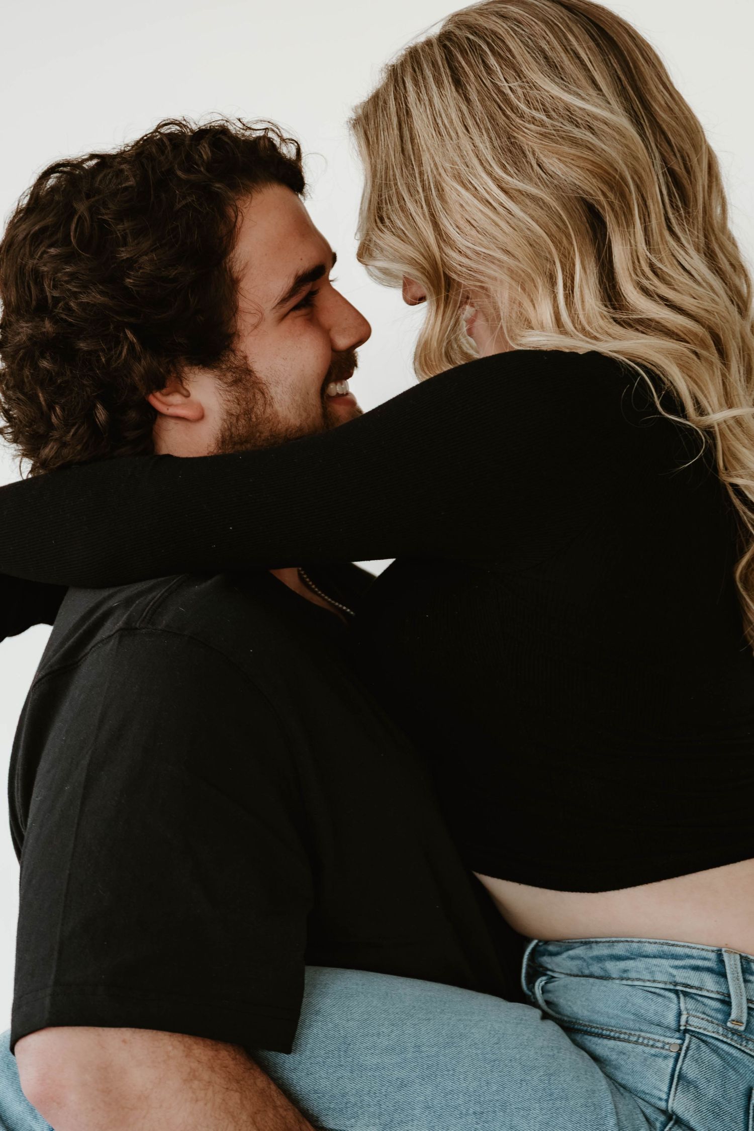 A couple in black clothing share an intimate moment against a light background.