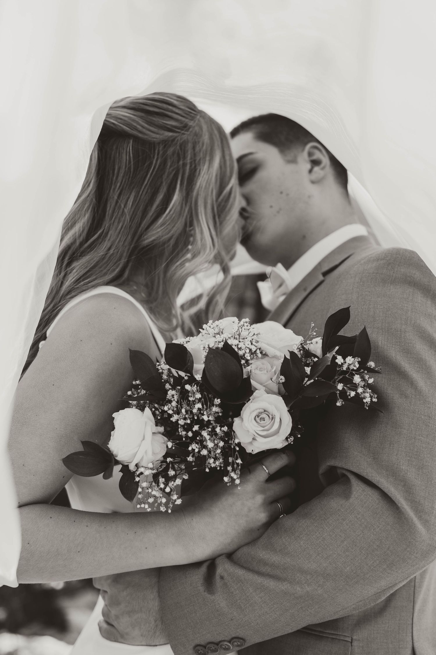A romantic black and white photo series showing five intimate wedding couple kisses with floral bouquet details.