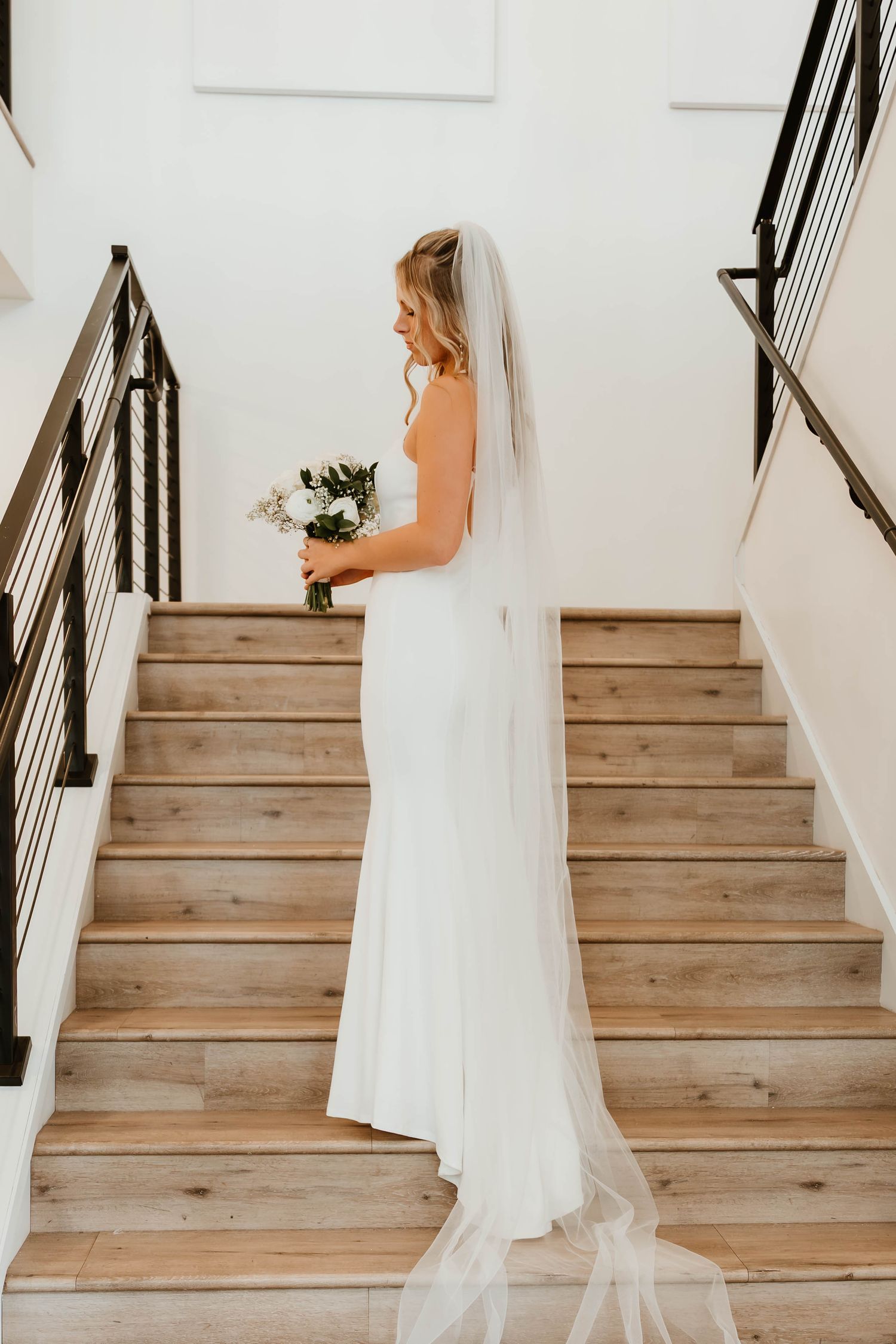 Elegant white wedding dress photographed on wooden staircase with natural lighting.