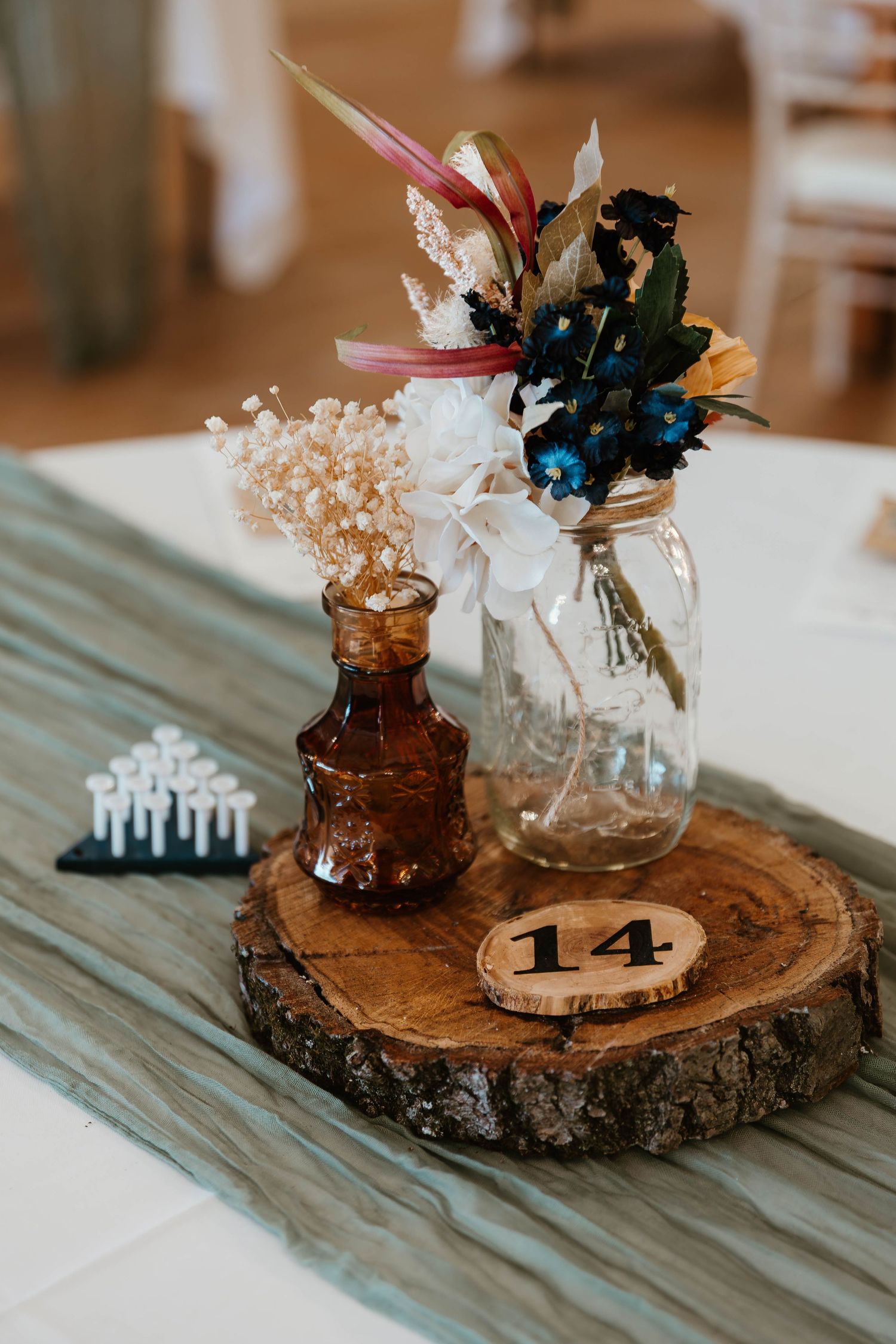 Rustic wedding table centerpieces featuring wood slices, mason jars, and dried flowers with table numbers.