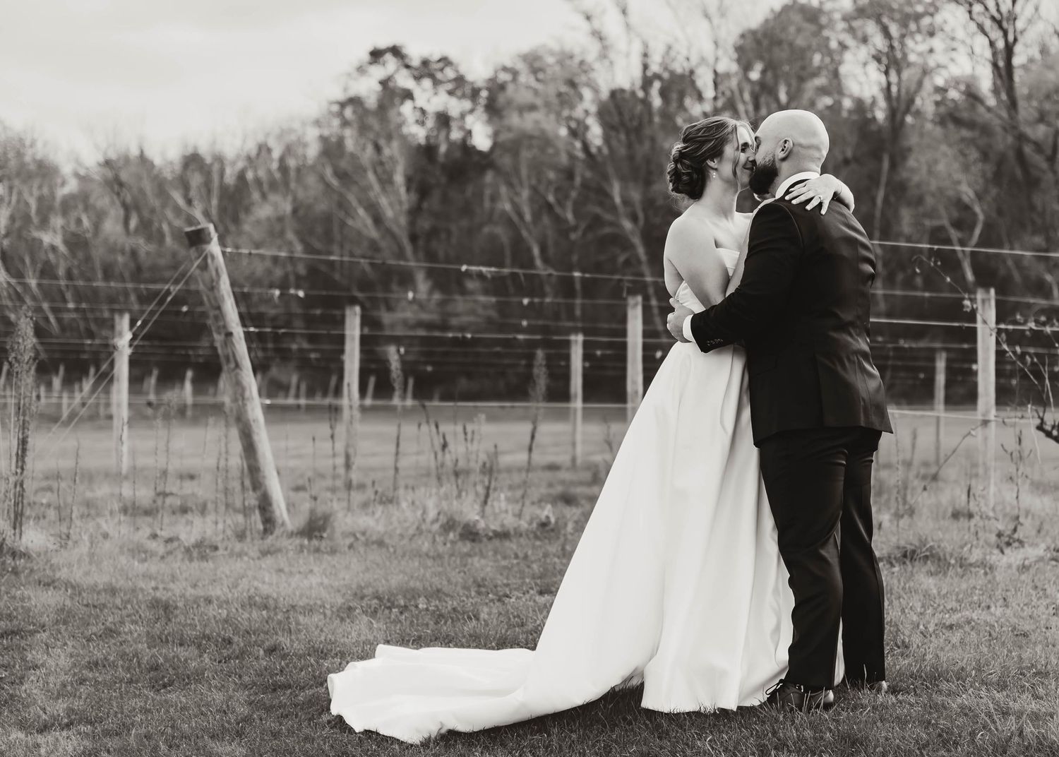 A black and white wedding photo series capturing intimate moments between newlyweds in a pastoral field setting.