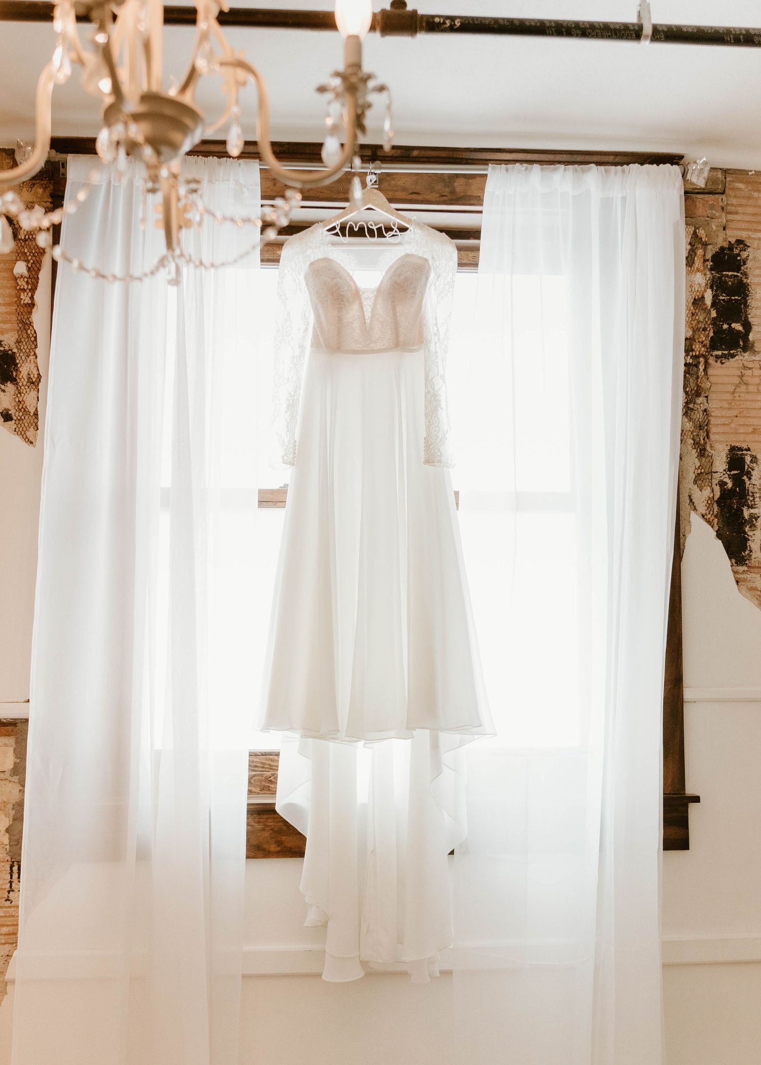 White wedding dresses hanging from wooden beams in a rustic venue with exposed brick walls.