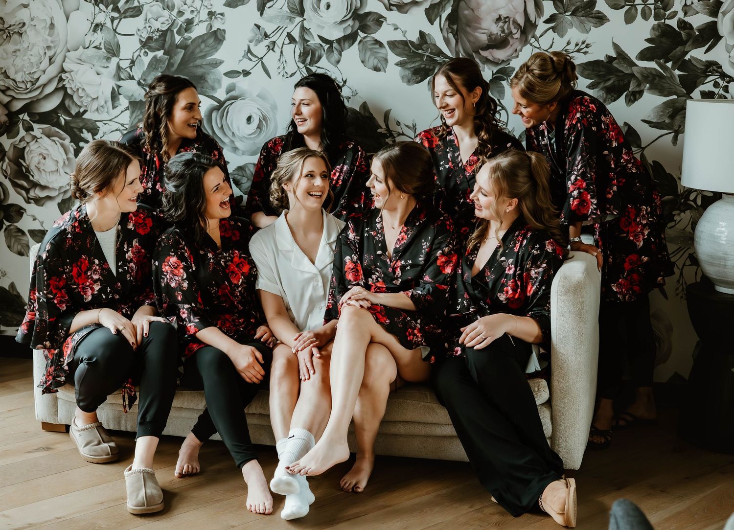 Group relaxing on floor in matching floral robes during wedding preparation.