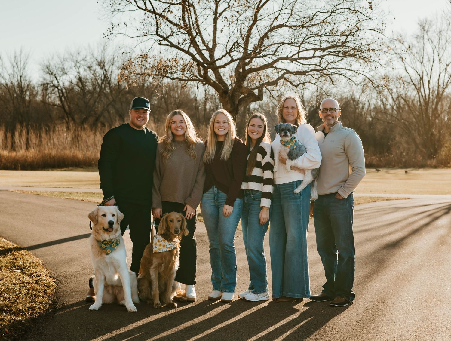A group of people standing together outdoors at sunset, wearing casual clothing in coordinated blue and neutral tones.