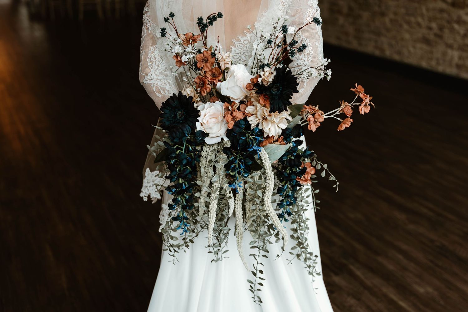 Close up of bridal bouquet with white dress against dark wooden floor.