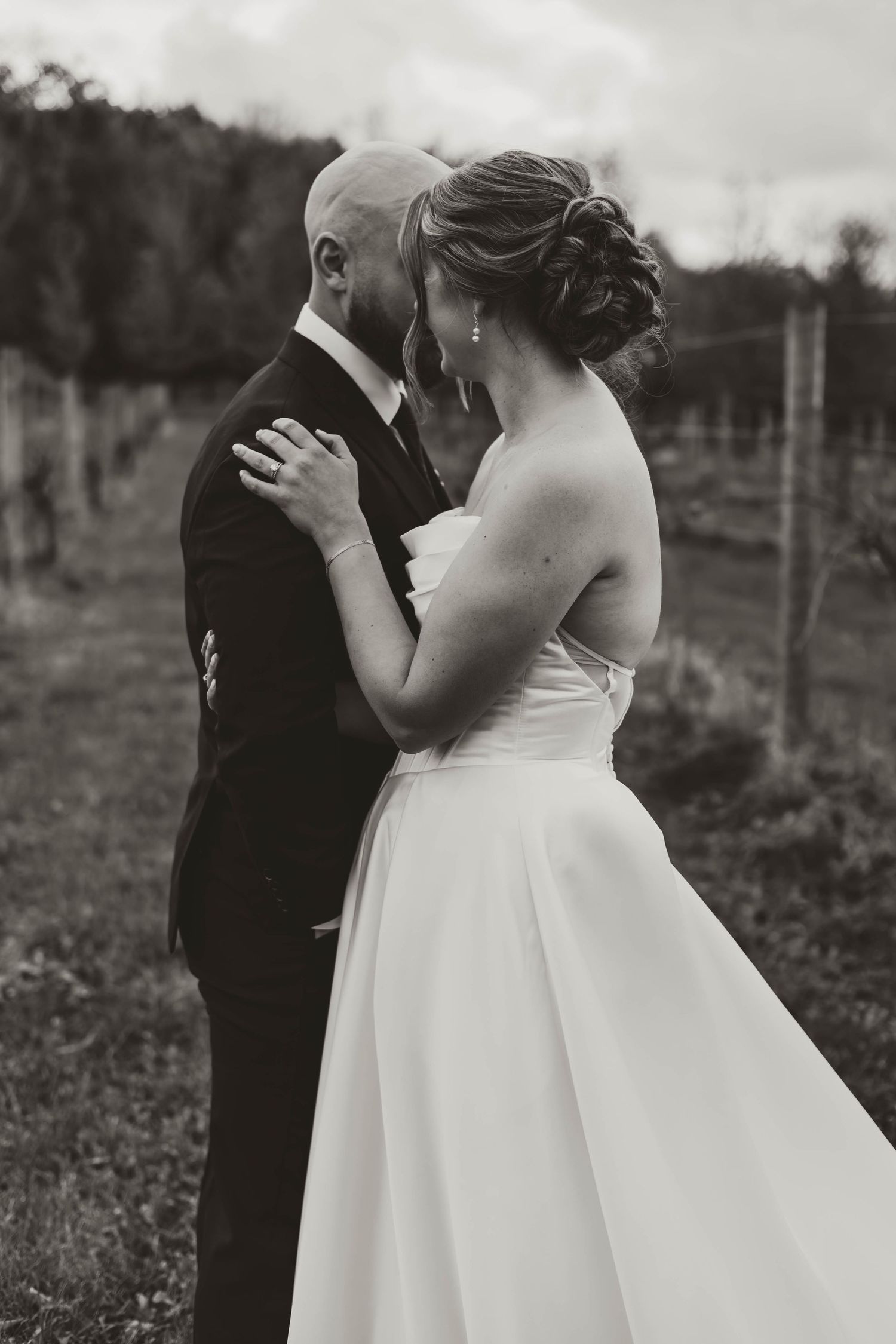 A romantic black and white portrait of a couple embracing in formal wedding attire outdoors.