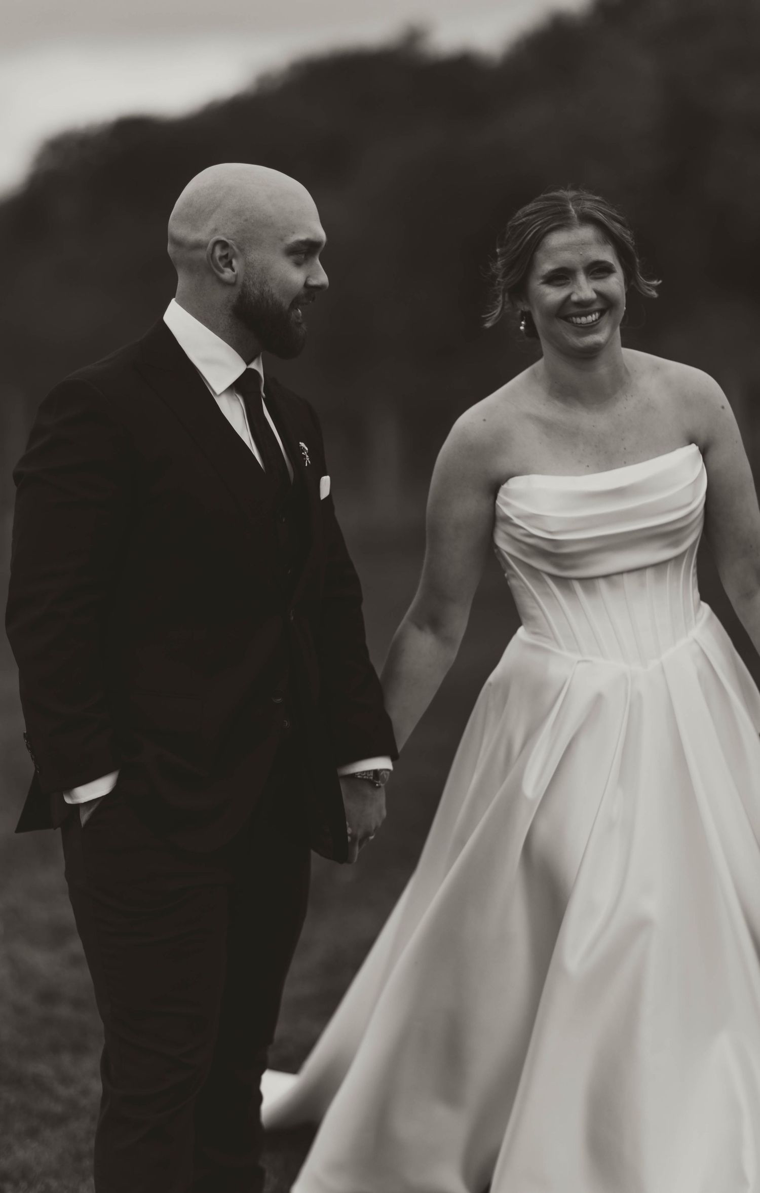 Black and white candid wedding photo of couple walking together outdoors.