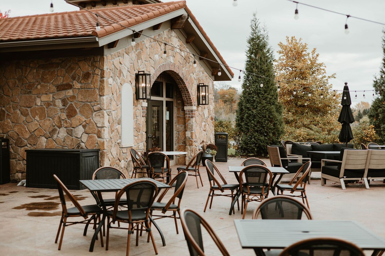 Rustic outdoor venue with string lights and terrace seating under a tiled roof.