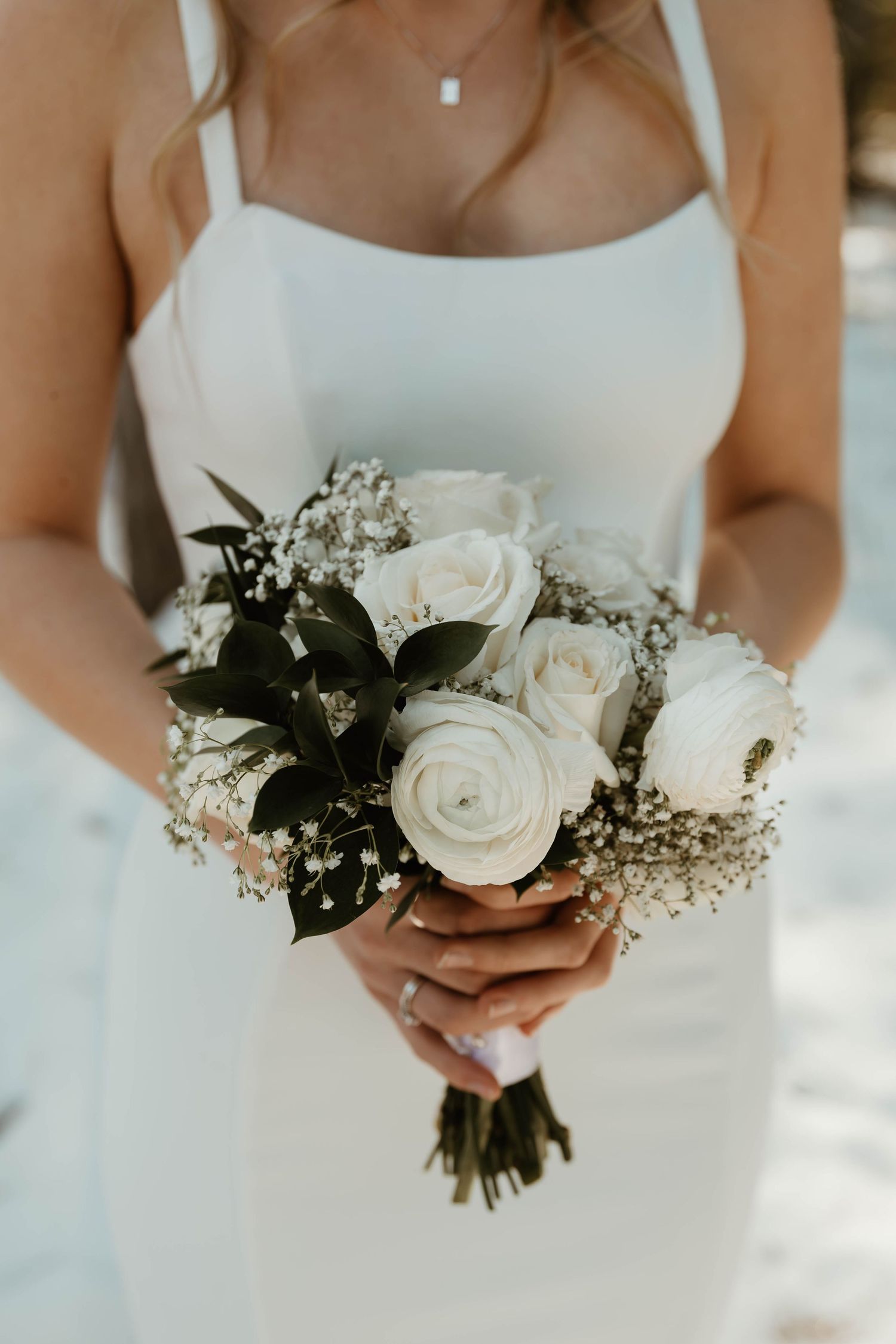 Elegant bridal bouquet featuring white roses and baby's breath against a white dress.