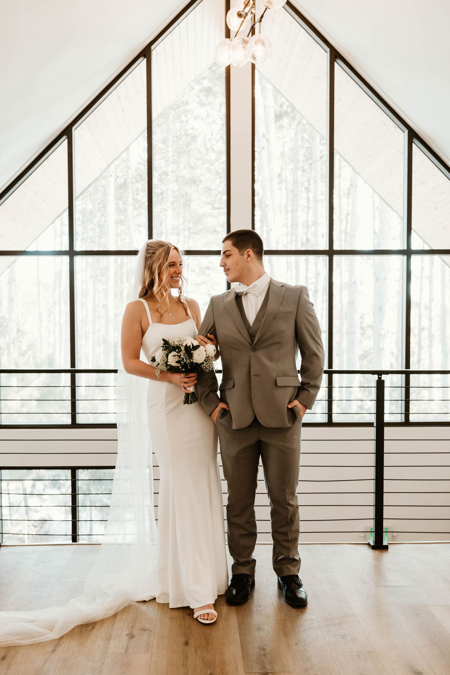 Modern wedding venue features floor-to-ceiling windows and minimalist white walls with couple in formal attire.