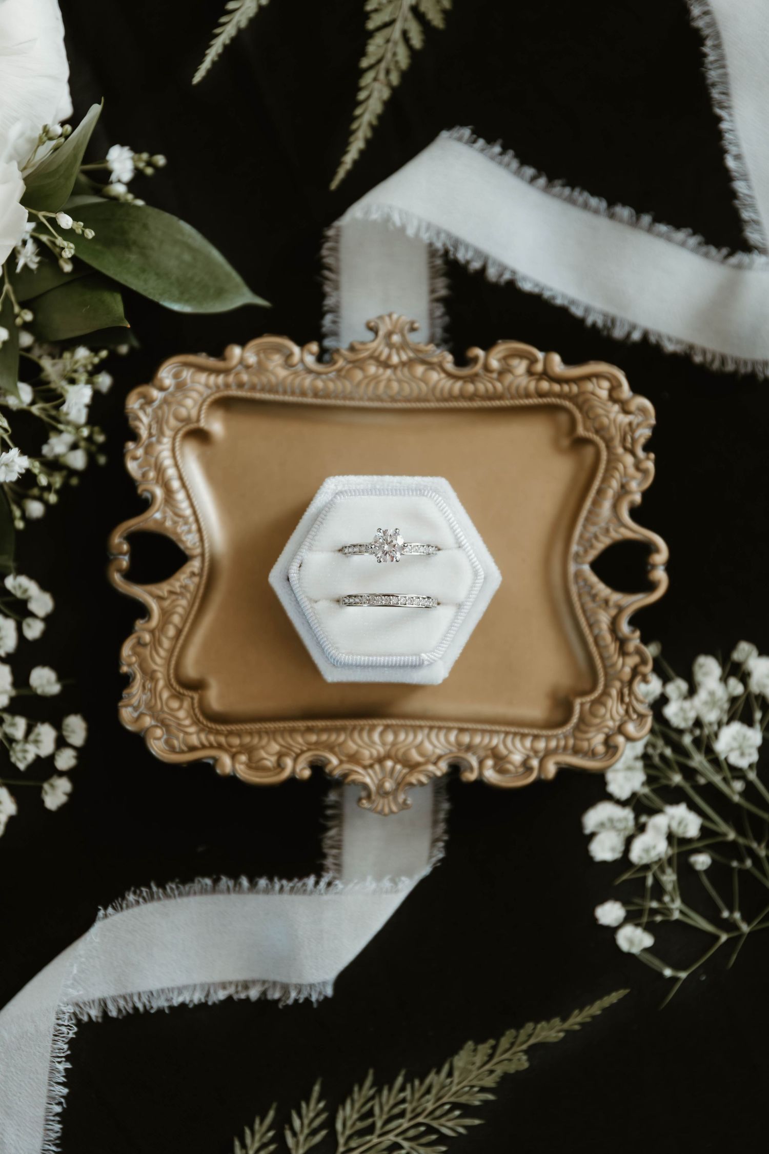 Wedding rings displayed on elegant gold decorative trays with white floral accents.