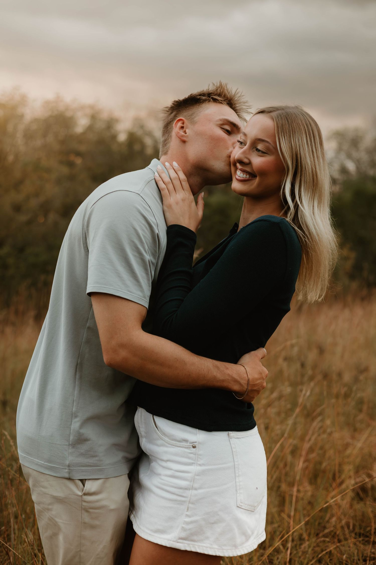 A romantic moment between a couple embracing in a field during golden hour.