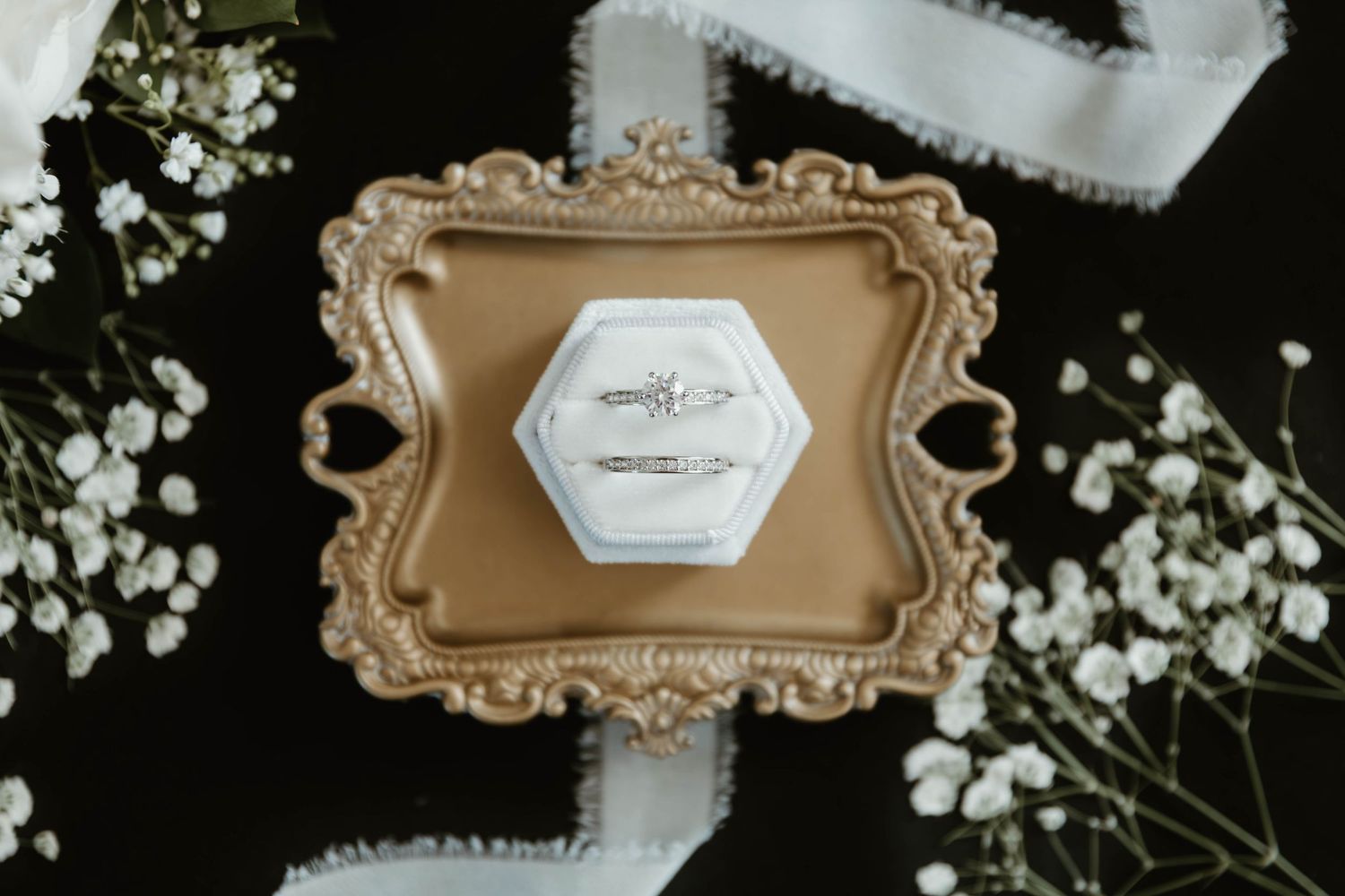 Elegant vintage-style table settings with white floral arrangements and ornate gold frames on a dark background.