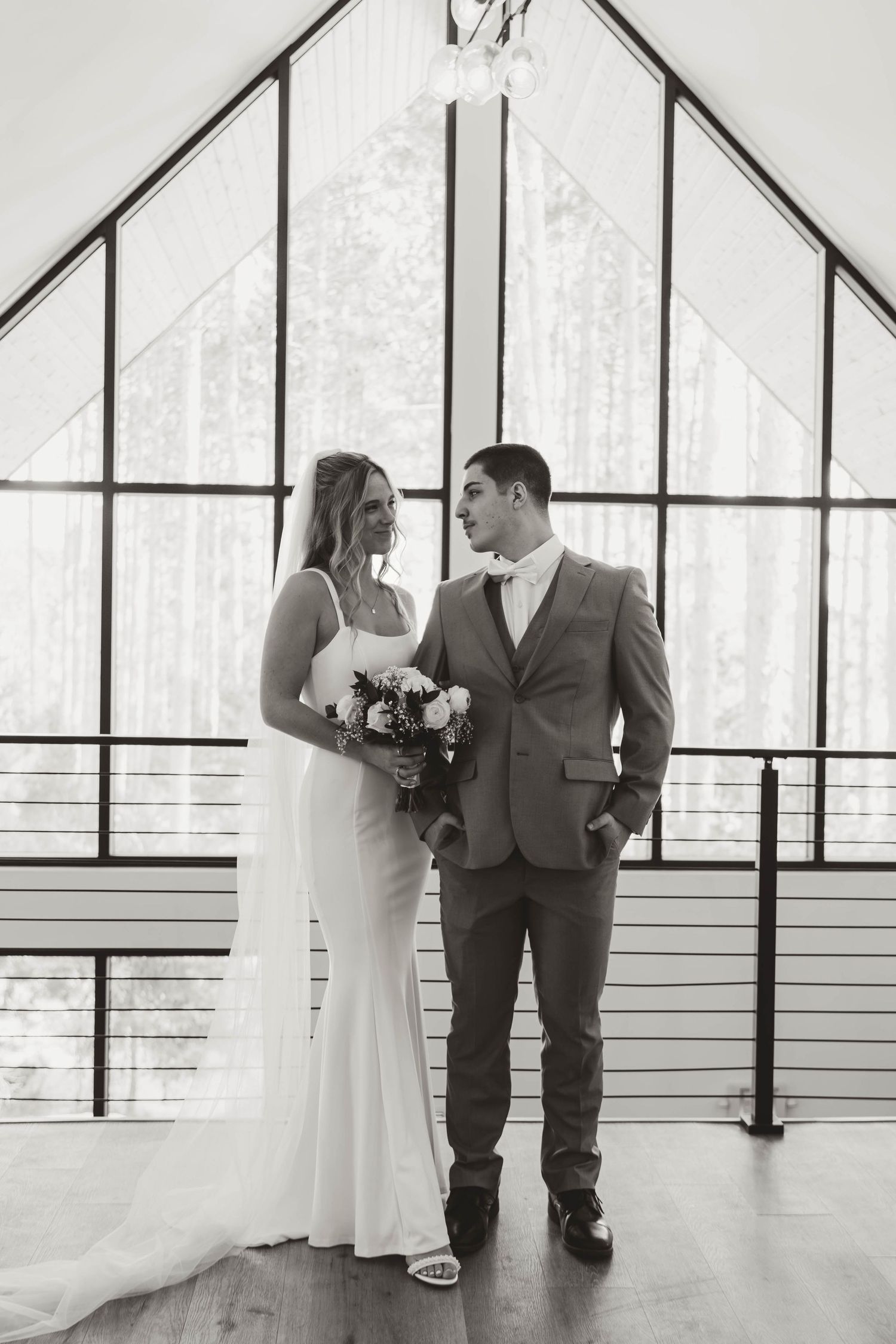 Wedding couple standing in modern chapel with floor-to-ceiling windows.