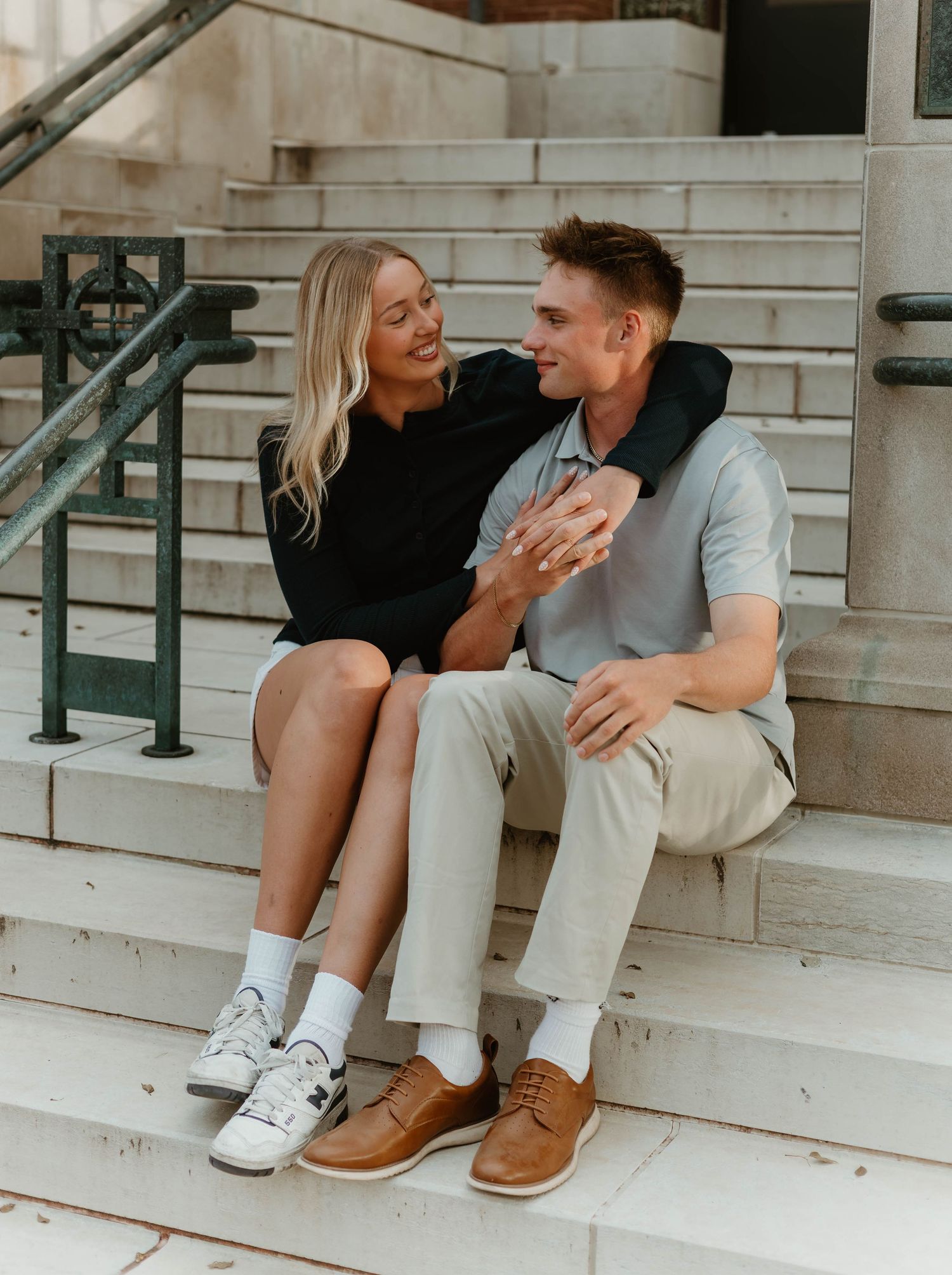 Couple sitting casually on white stone steps wearing contrasting casual outfits and shoes.