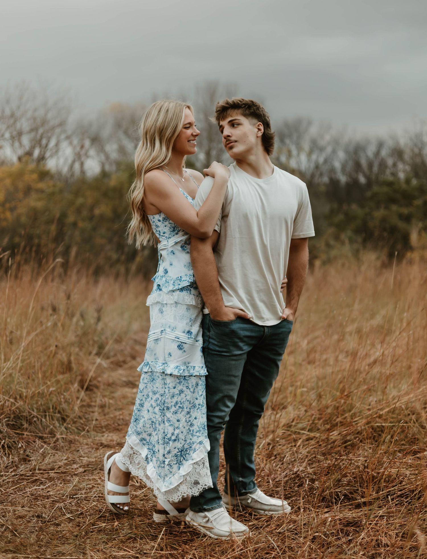 A romantic couple embraces while standing in tall grass during a dreamy outdoor photoshoot.