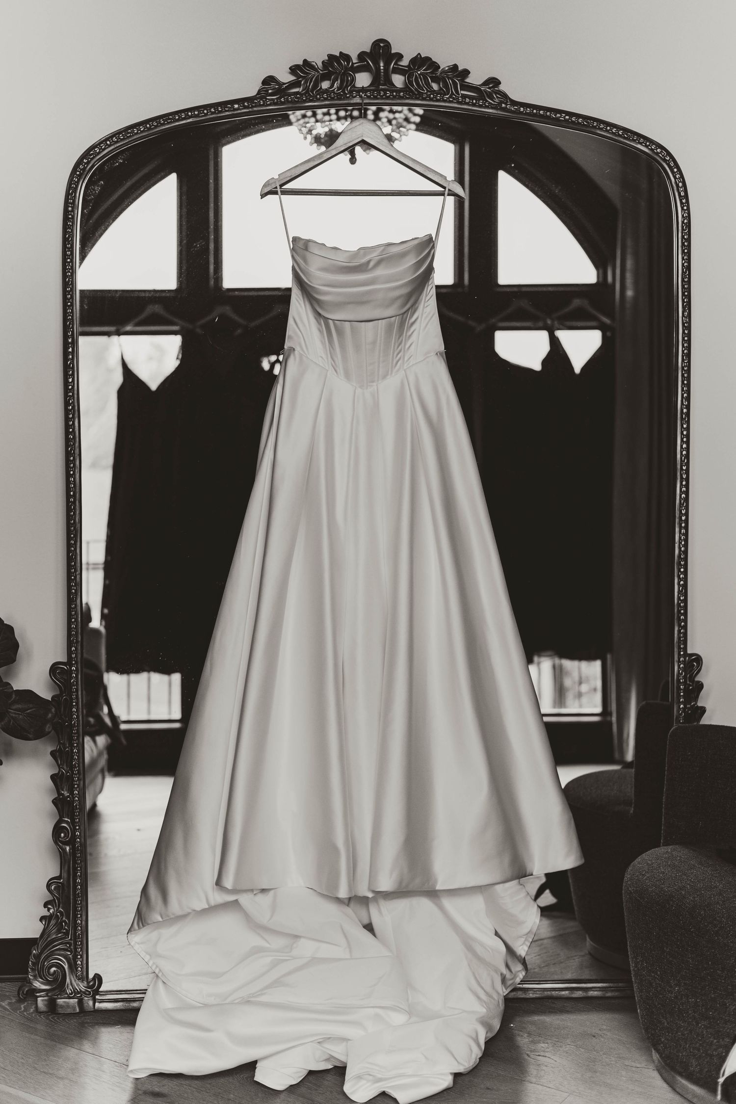 An elegant white strapless wedding gown hangs on display in an ornate vintage mirror frame.