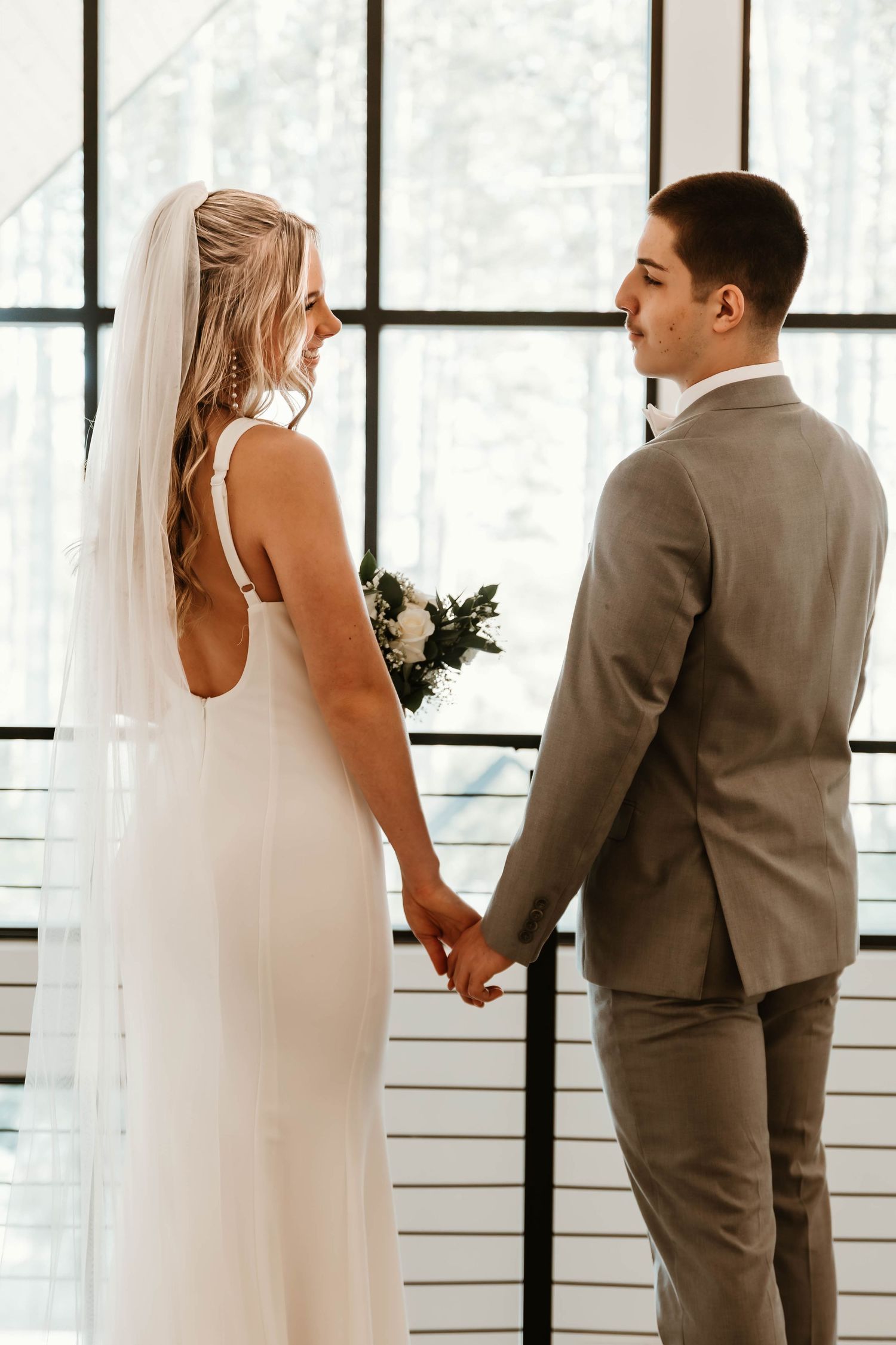 Romantic first look moment between newlyweds in front of large windows.