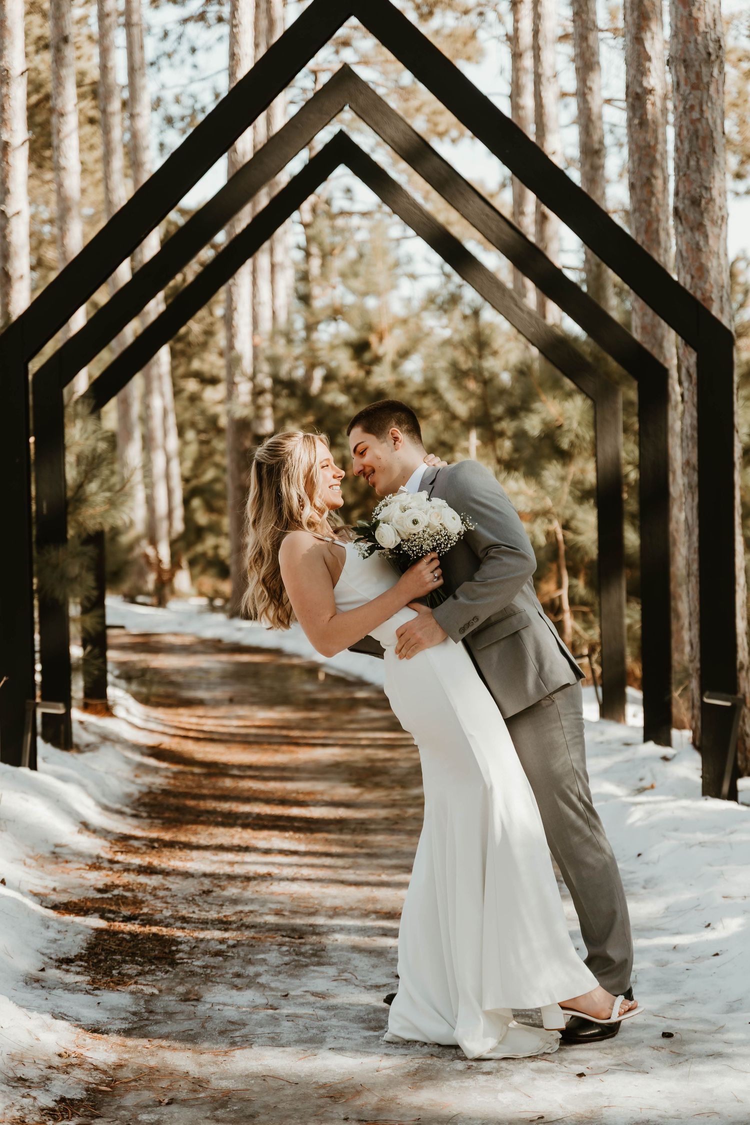 Romantic winter wedding photos under geometric black arches with snow-covered ground.