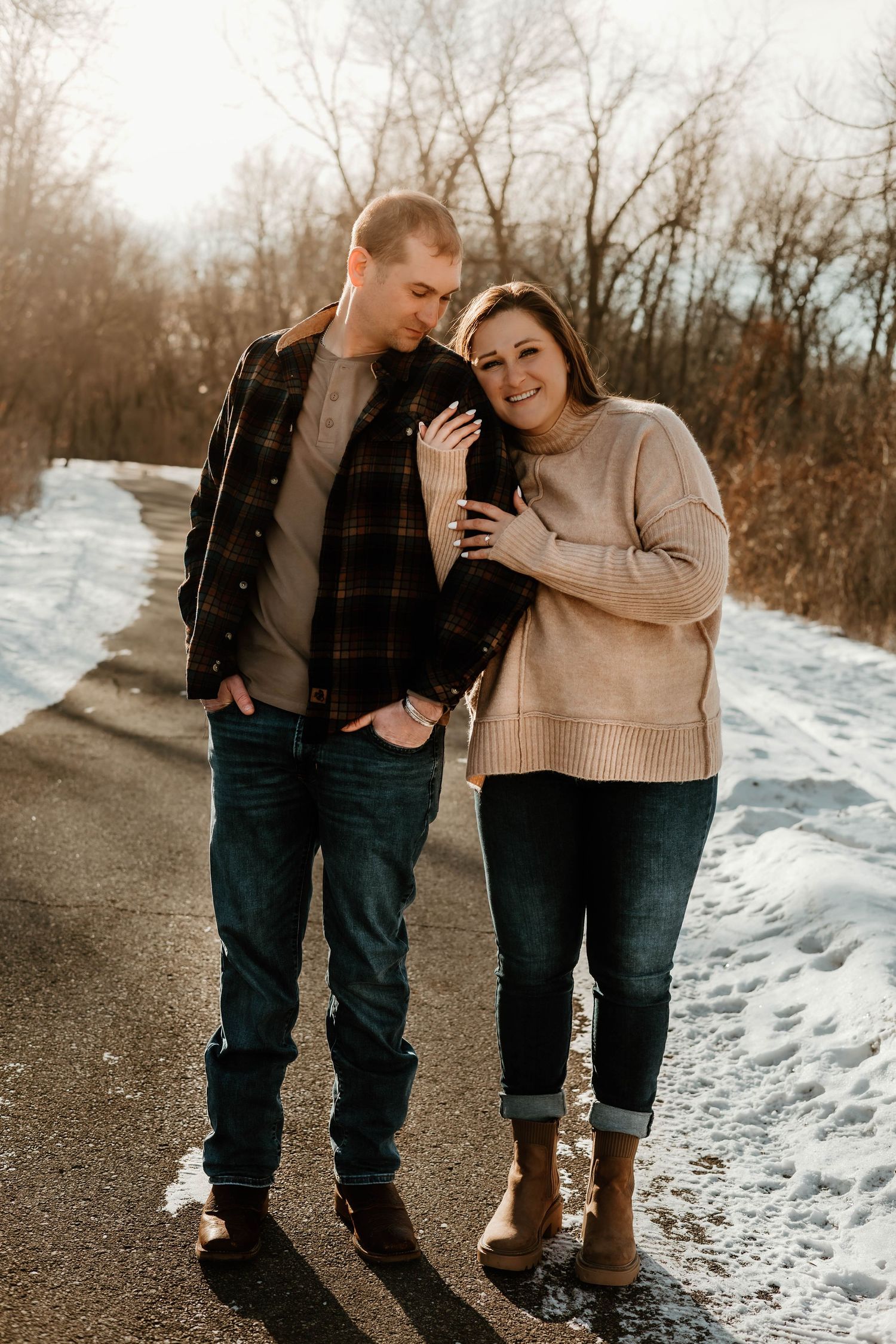Two people walk together on a snowy winter path wearing casual clothing and boots.
