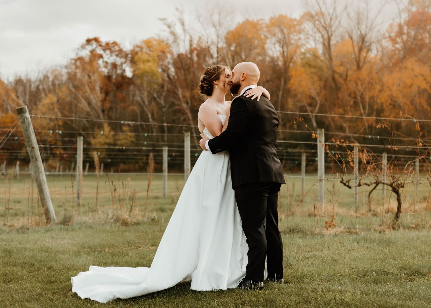 Couple embracing in field during golden hour with autumn foliage.