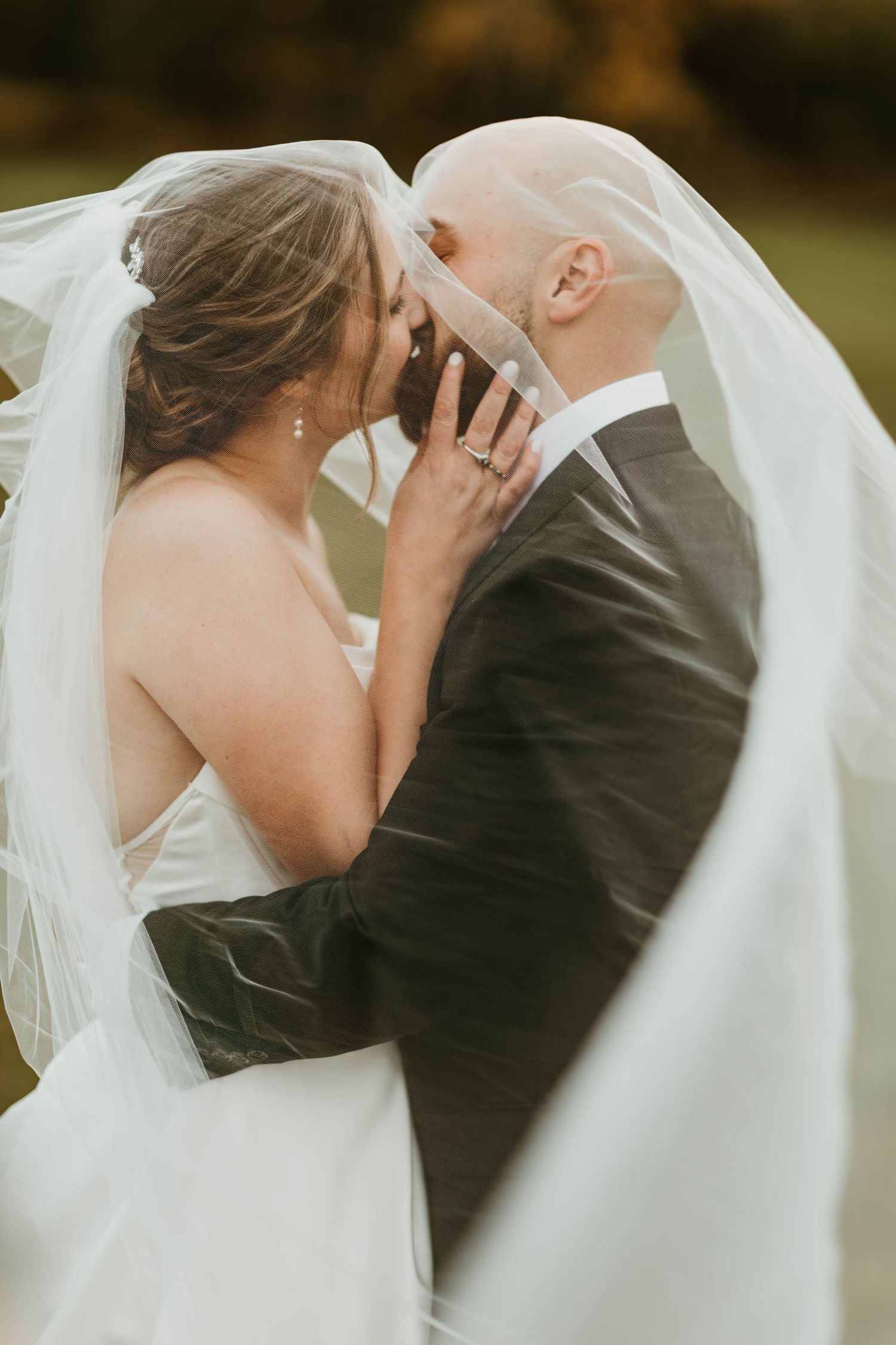 Romantic wedding moment captured with flowing white veil in natural outdoor setting.
