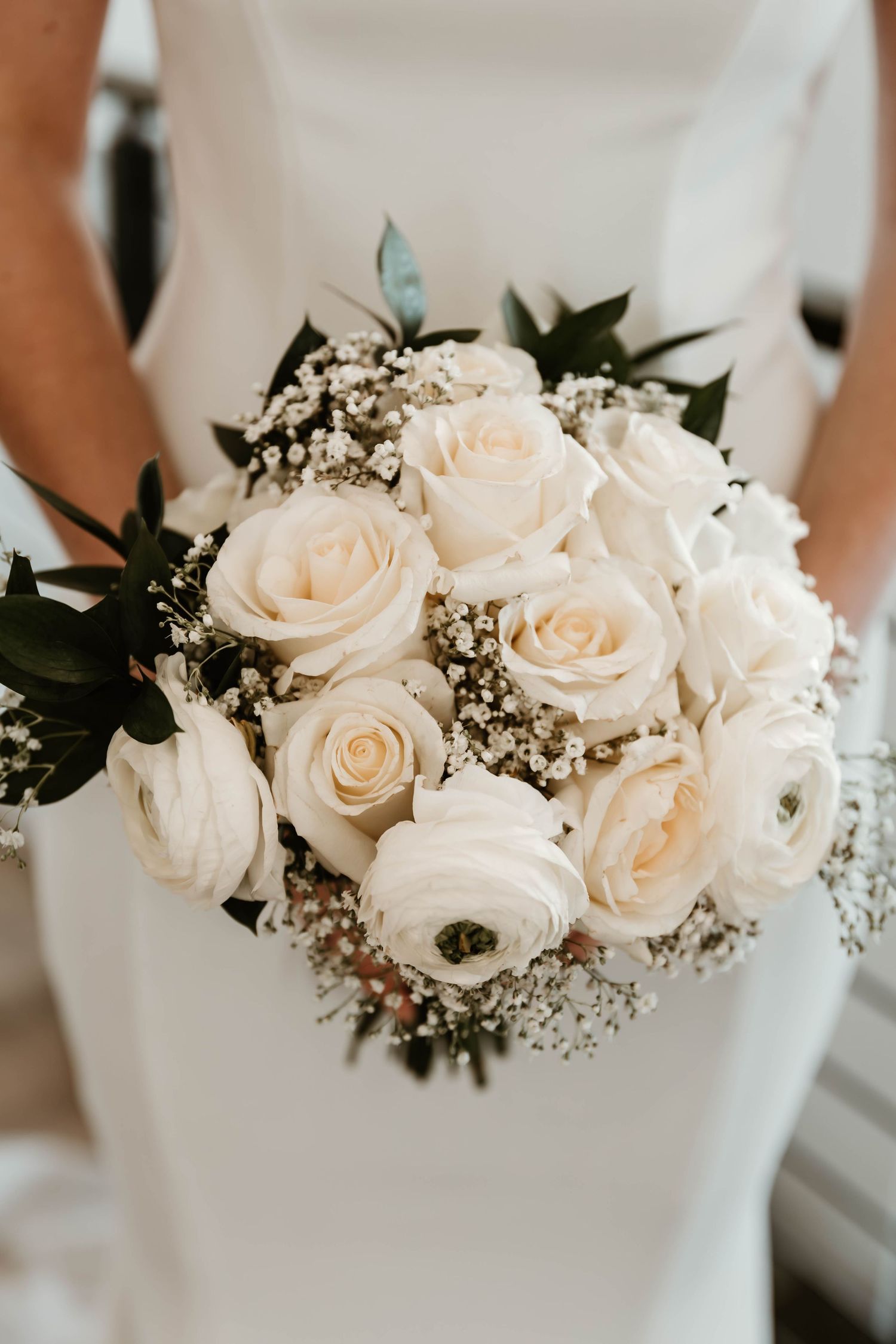 Elegant white rose and baby's breath wedding bouquet held against a white dress.