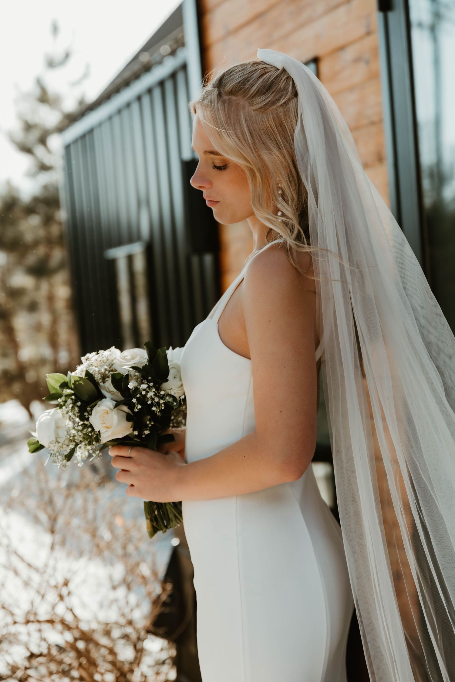 Elegant bridal portraits showing details of a flowing veil and classic white bouquet against wooden architecture.