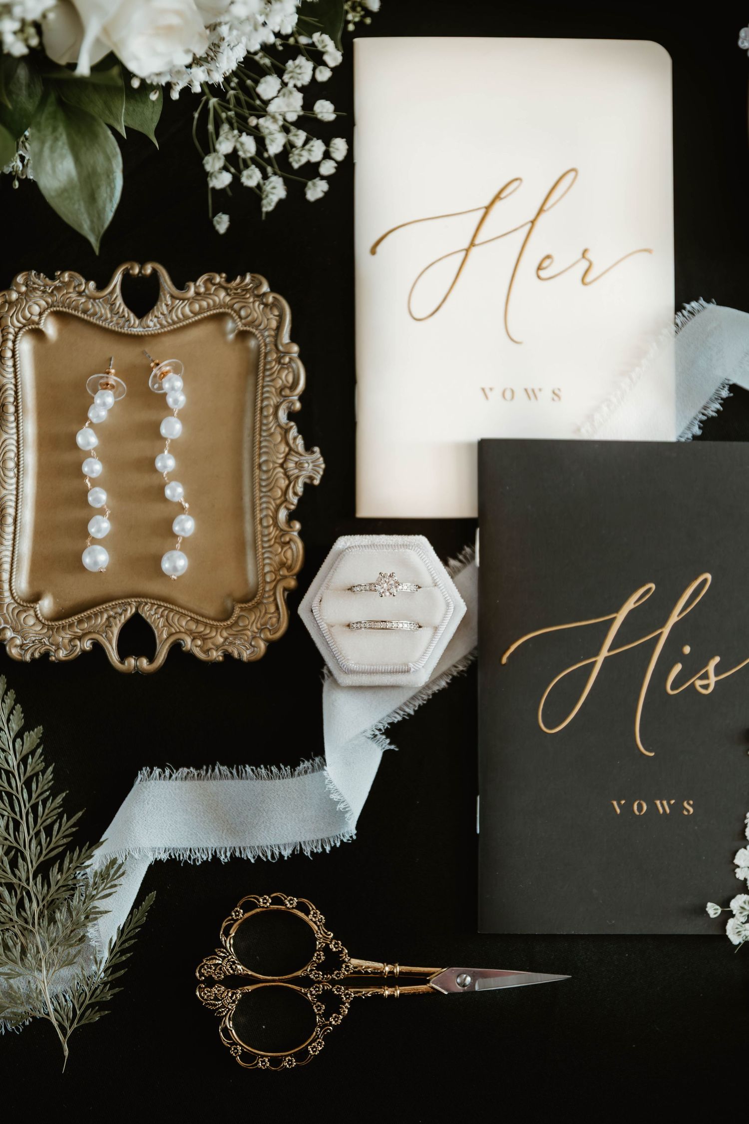 Wedding vows and bridal accessories including pearl earrings and ornate frames arranged in an elegant flat lay composition.