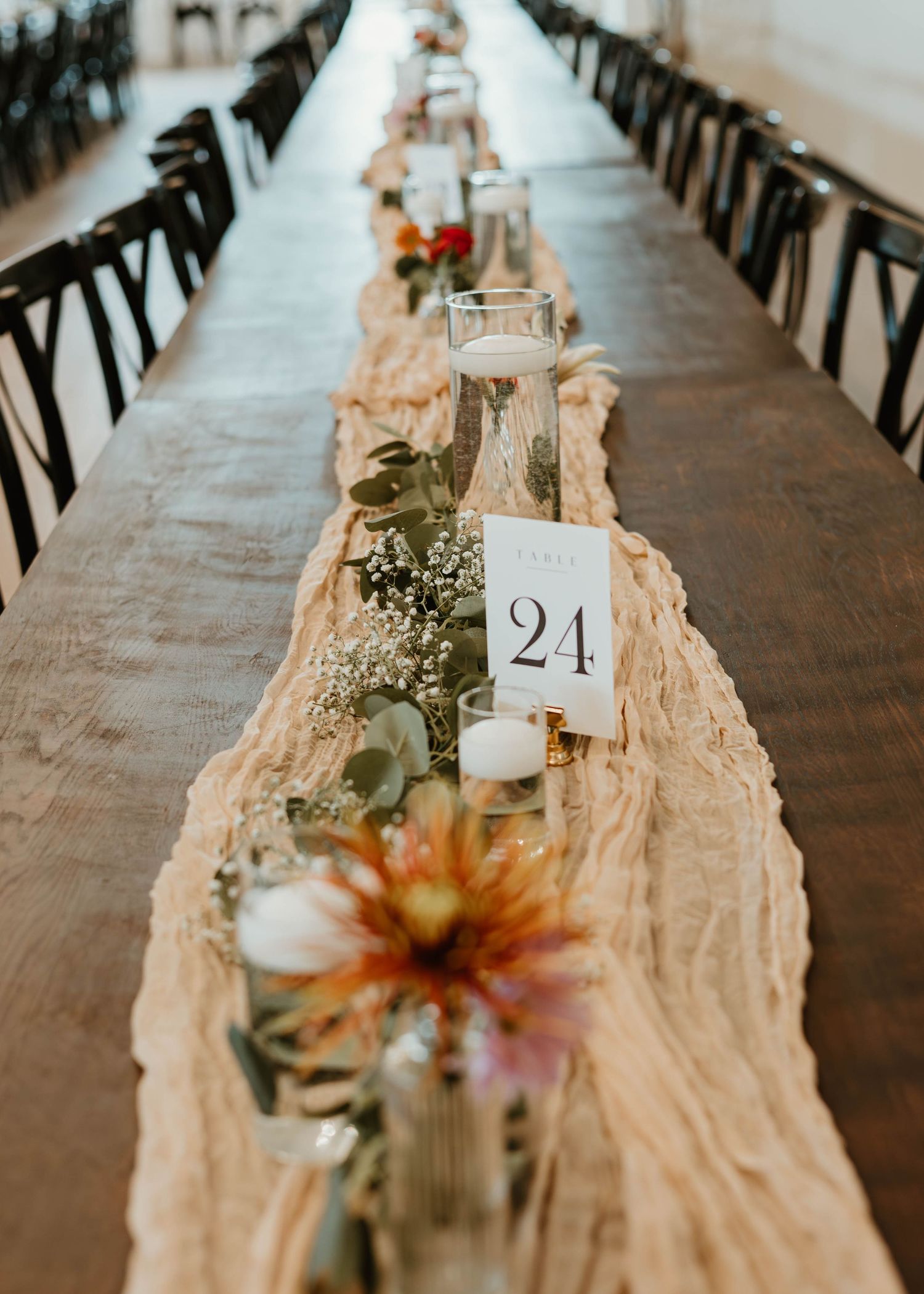 Long rustic dining table with table numbers and floral centerpieces.