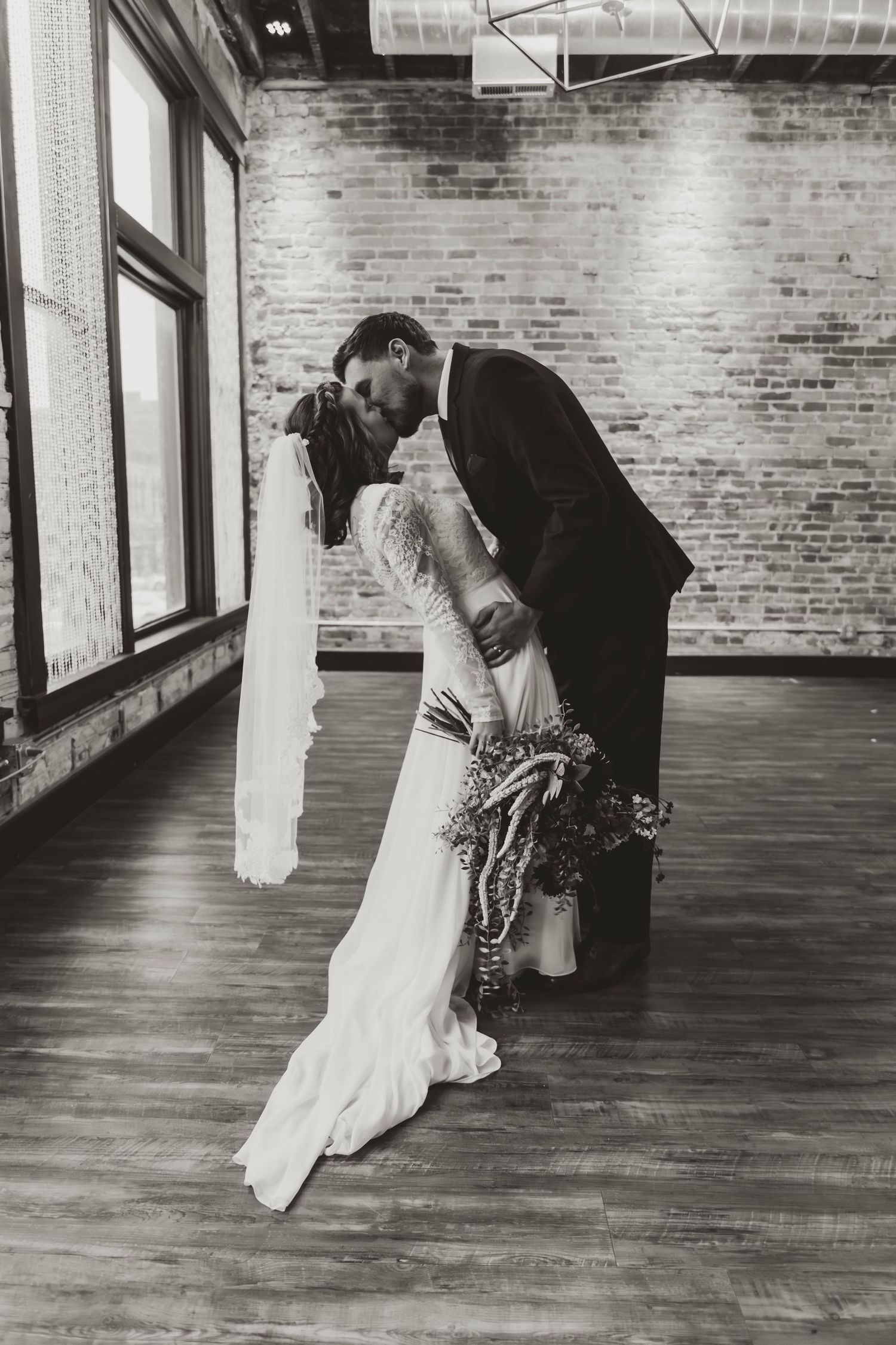 Romantic black and white wedding photo in industrial venue with hardwood floors.