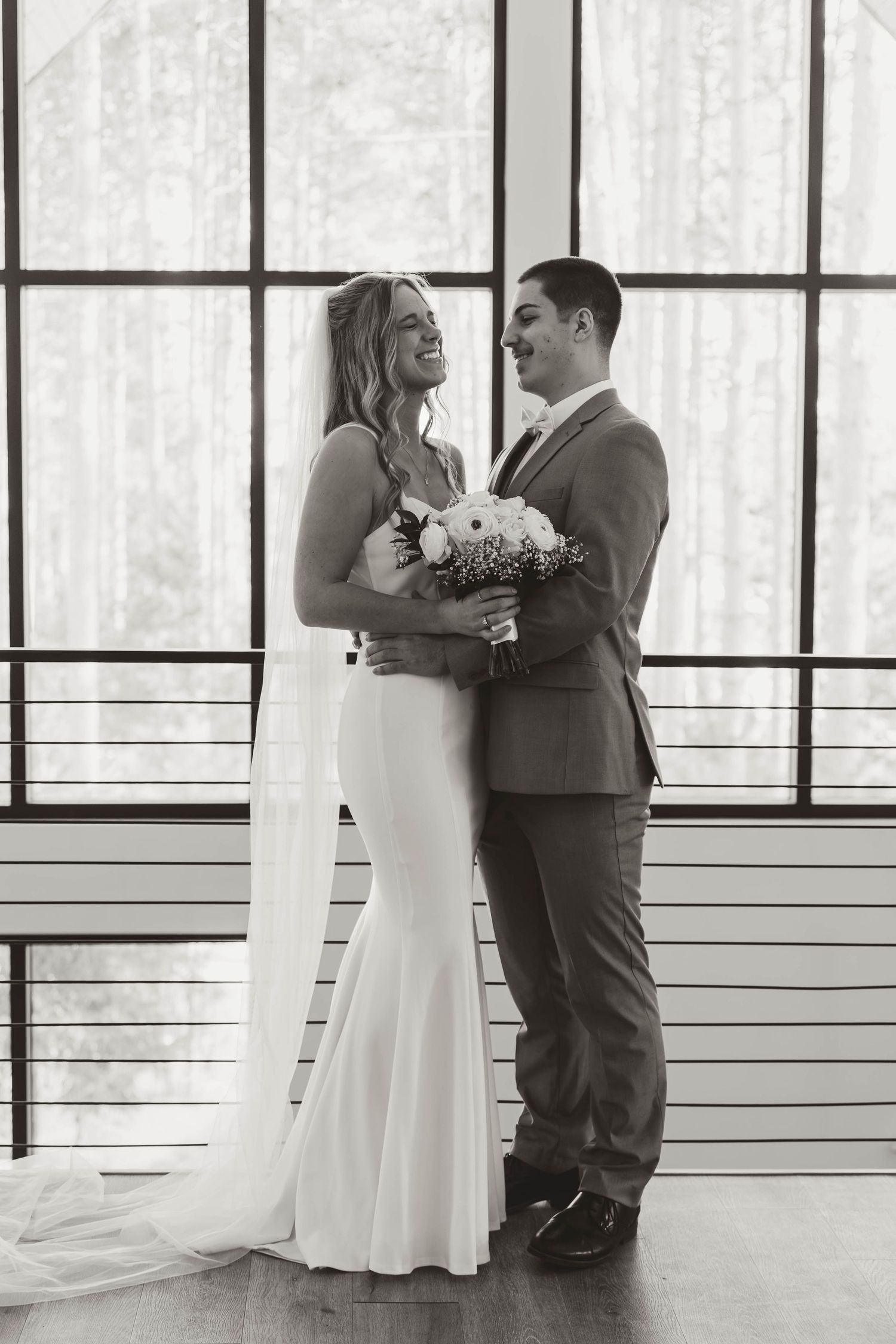 A romantic wedding portrait of a couple by large windows in black and white.