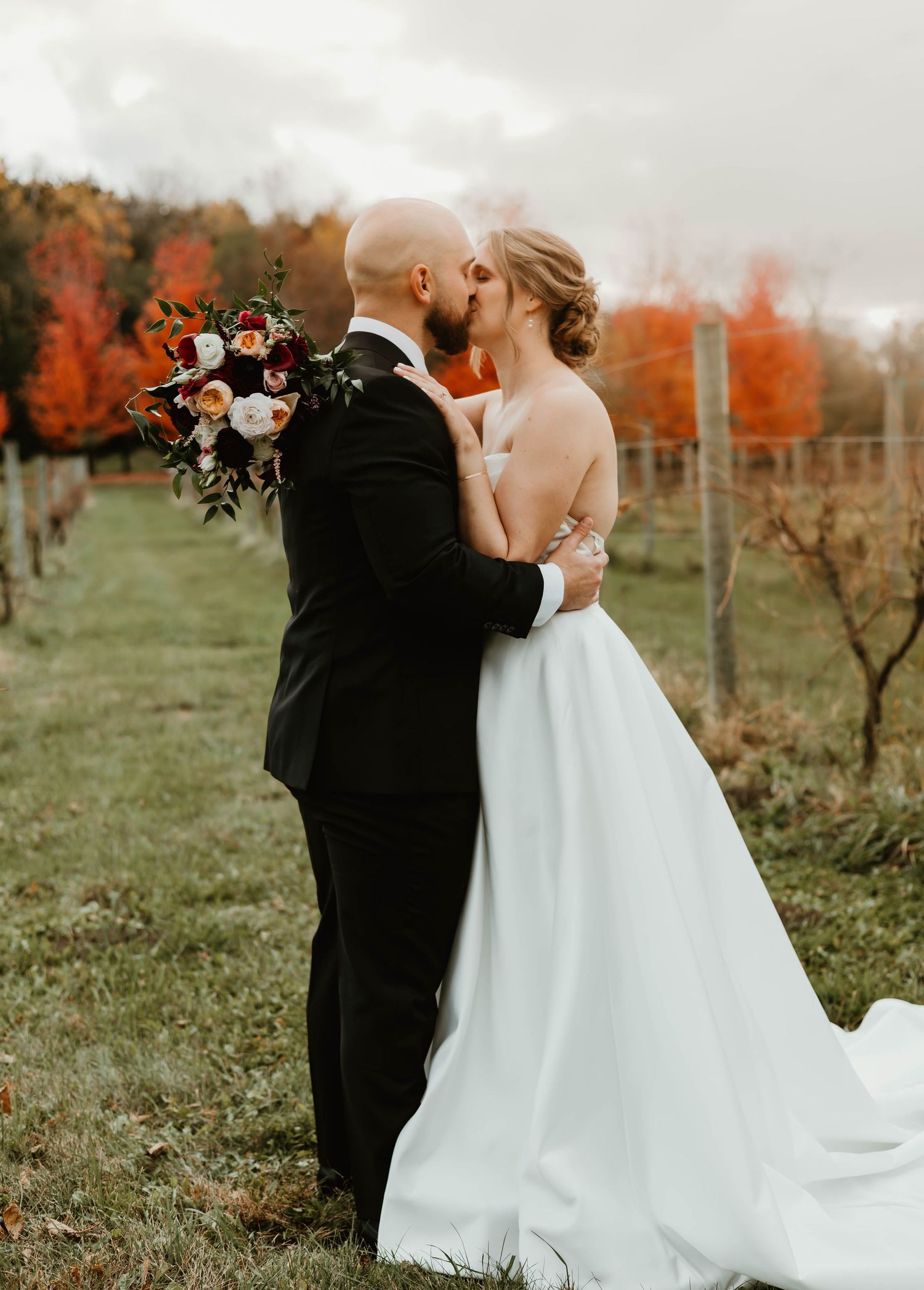 A couple shares their first kiss as newlyweds in front of vibrant fall colors.