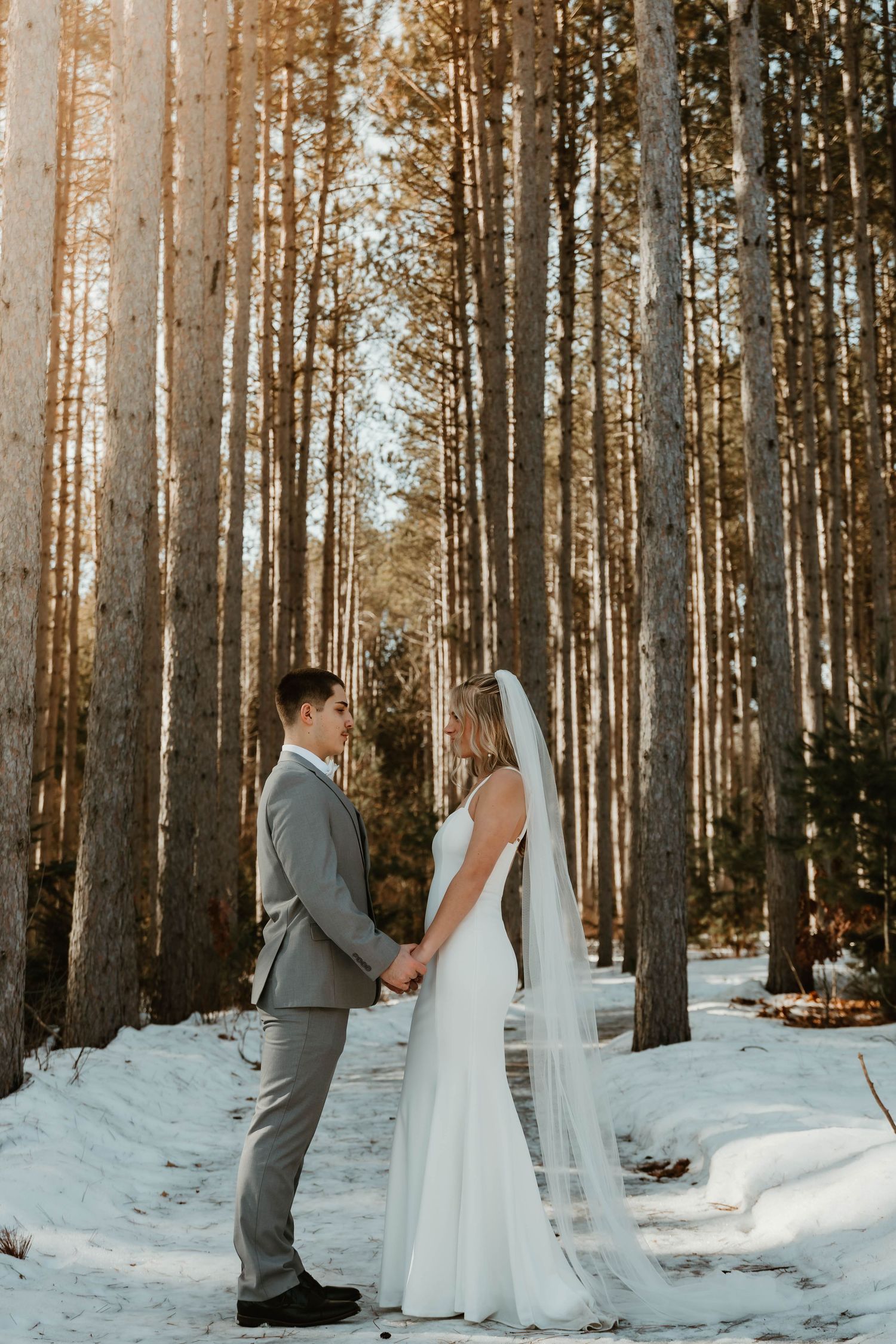 Romantic winter wedding photos of couple in snowy forest with tall pine trees.