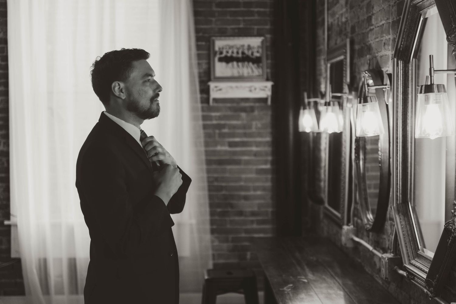 Silhouette of couple standing by window in brick venue with white curtains.