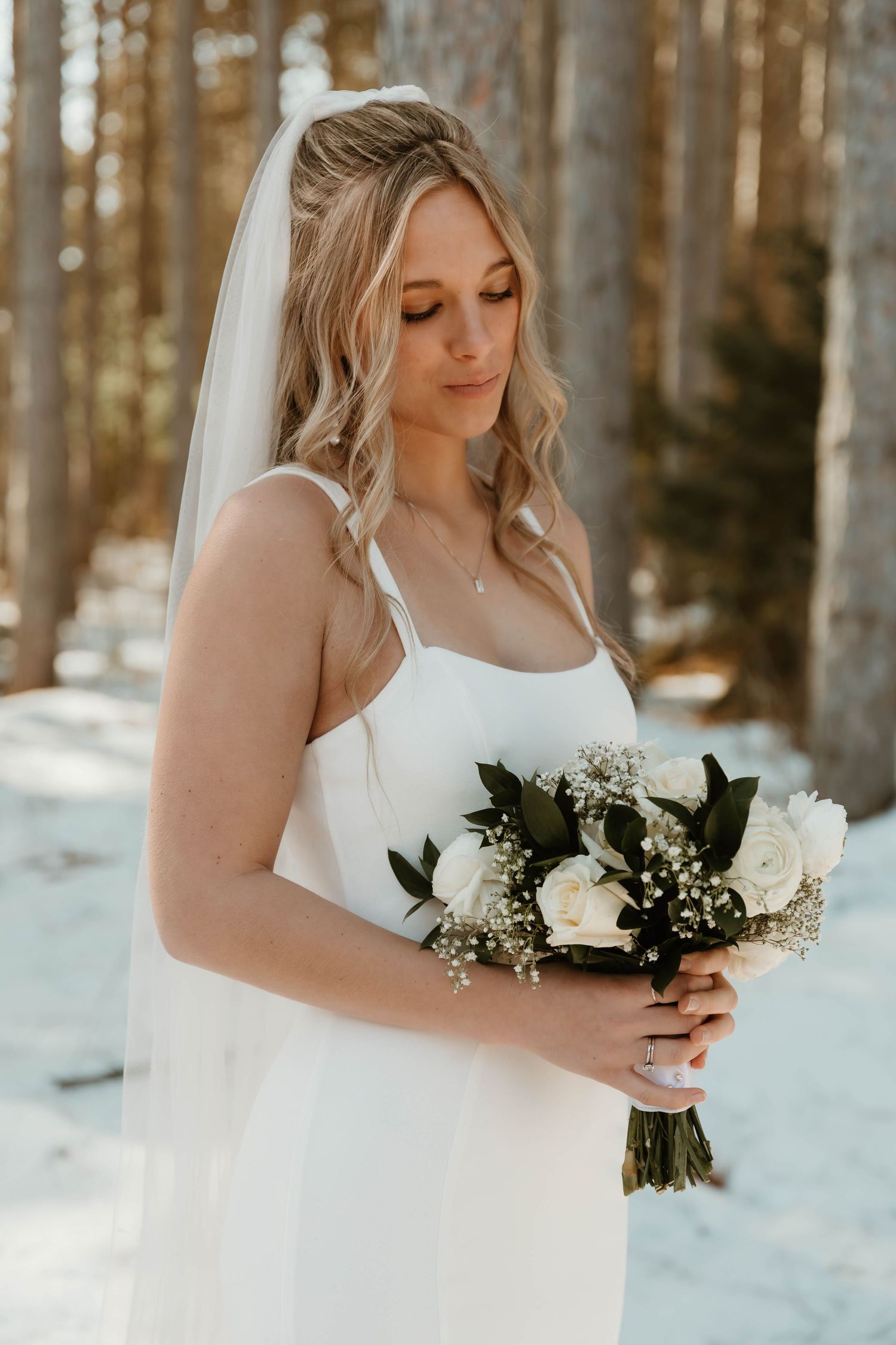 Winter bride holding a white and green bouquet against a snowy forest backdrop.