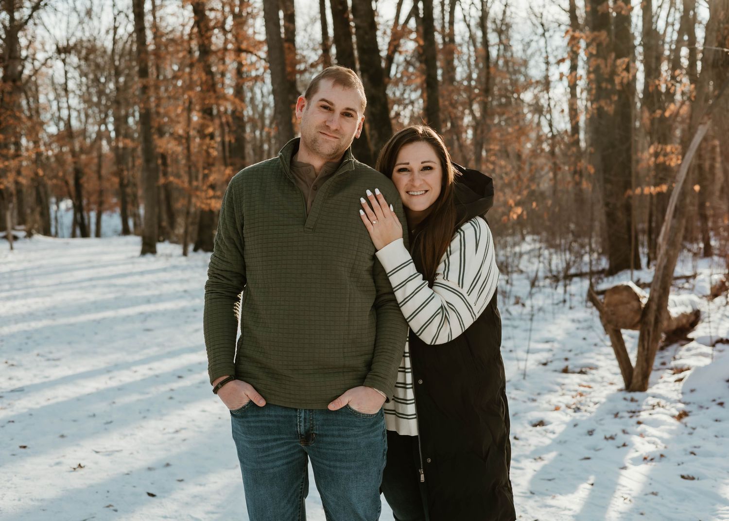 Couple in winter attire poses together on a snowy forest path during a cold winter day.