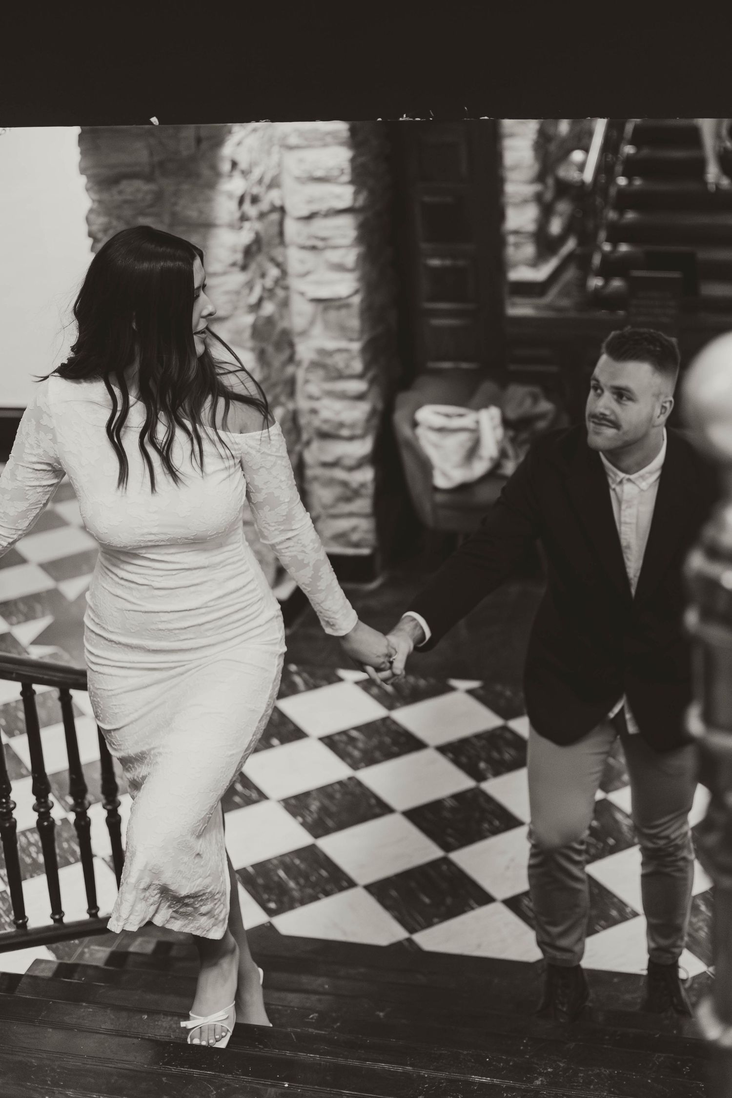 Close-up of bride's white dress and bare feet as she dances on a checkered floor.