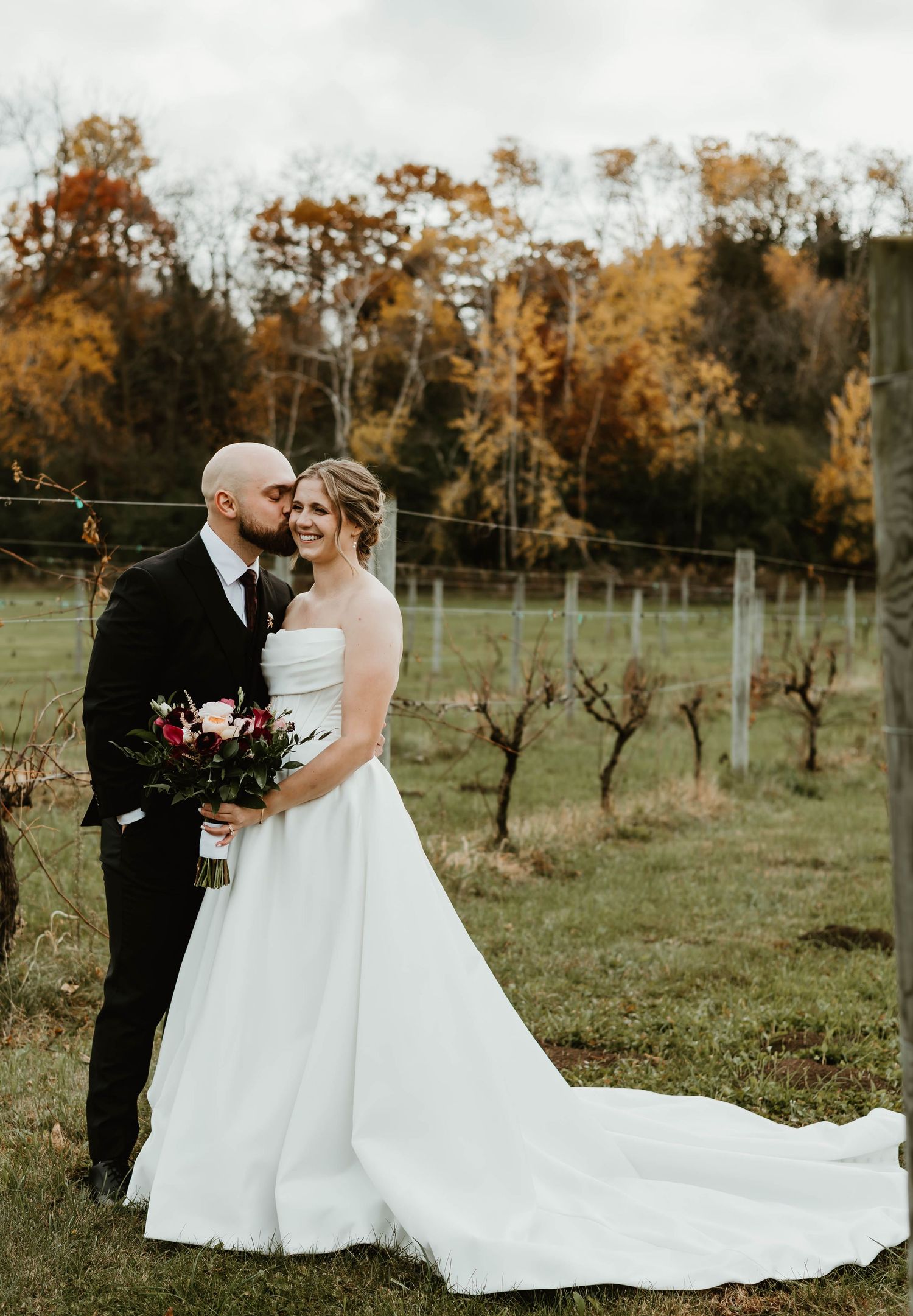 Romantic autumn wedding photos in a vineyard with bride's dress trailing beautifully on grass.