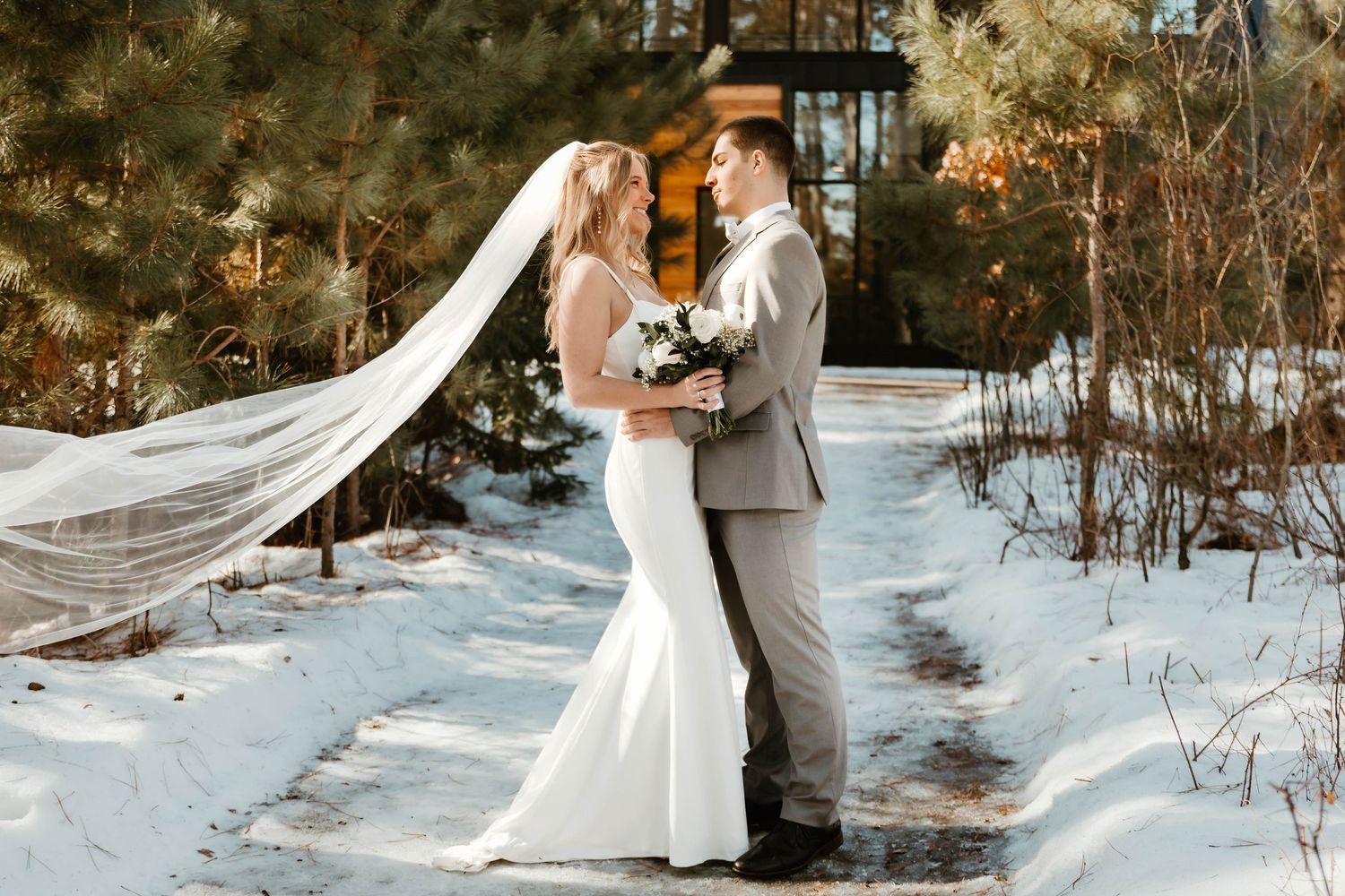 Winter wedding portraits in snow with A-frame chapel and flowing veil.
