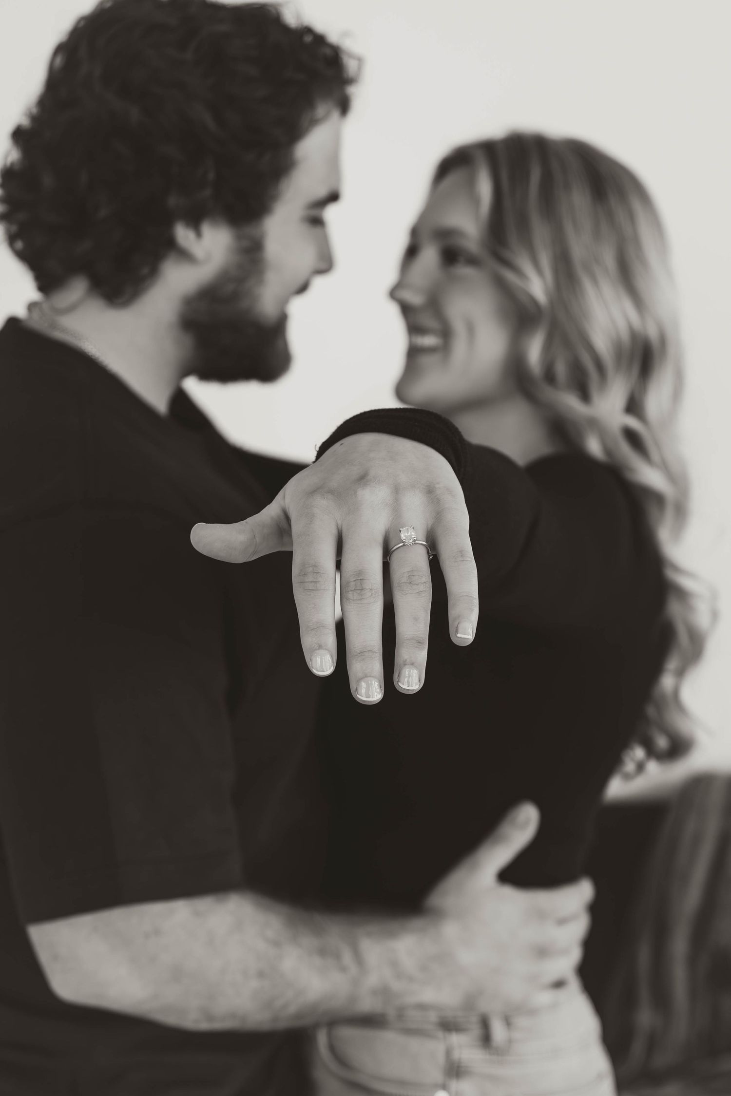 A black and white engagement photo showing a close embrace and ring display.