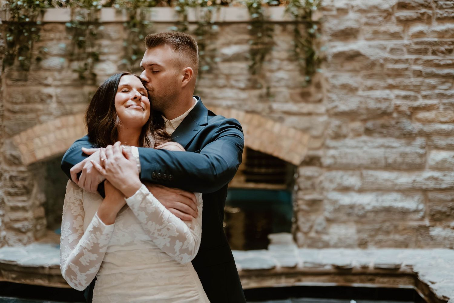 A romantic moment captured against a rustic stone wall backdrop during a wedding photoshoot.