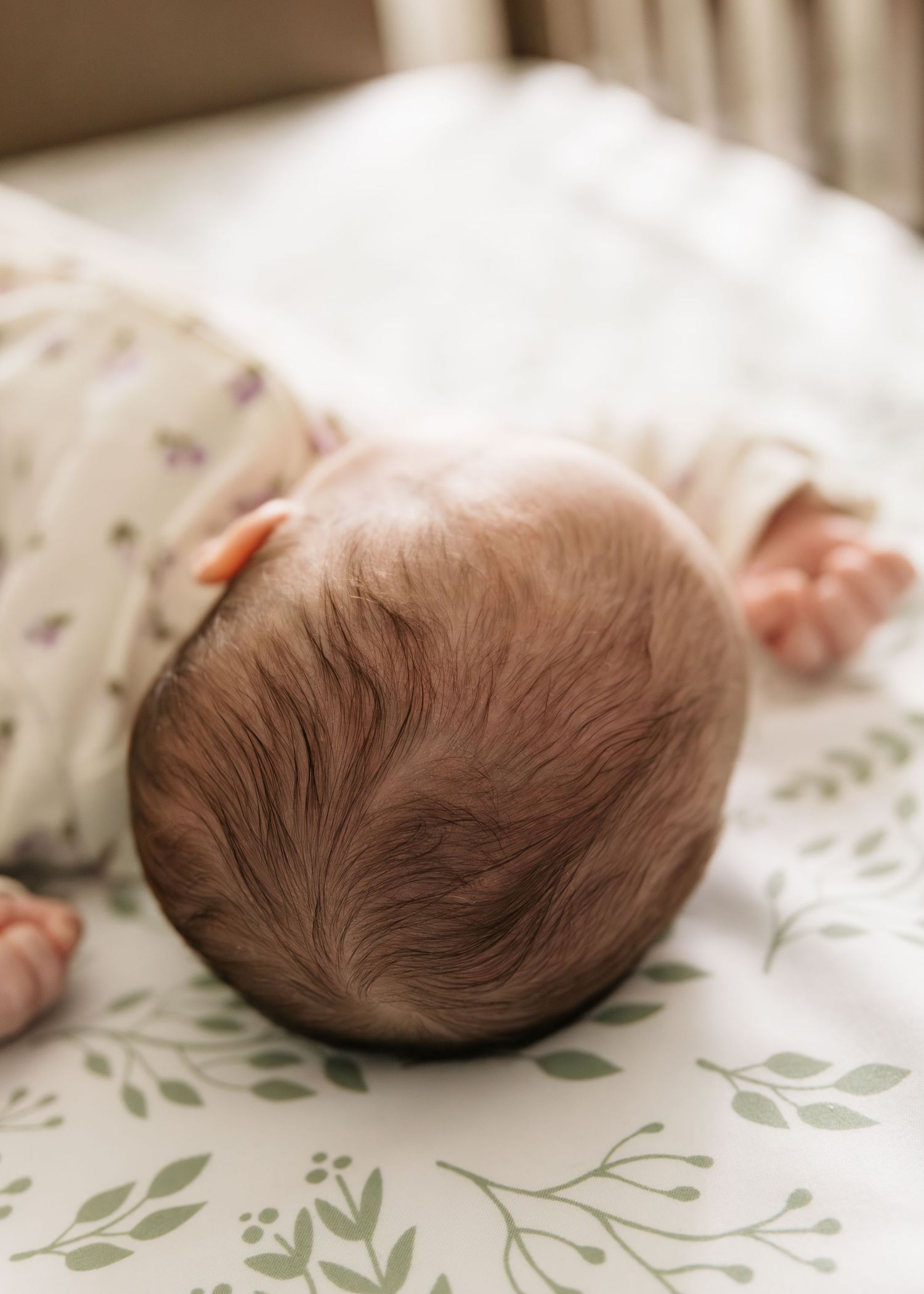 Newborn baby sleeping peacefully in a crib on floral sheets, viewed from above showing soft hair.