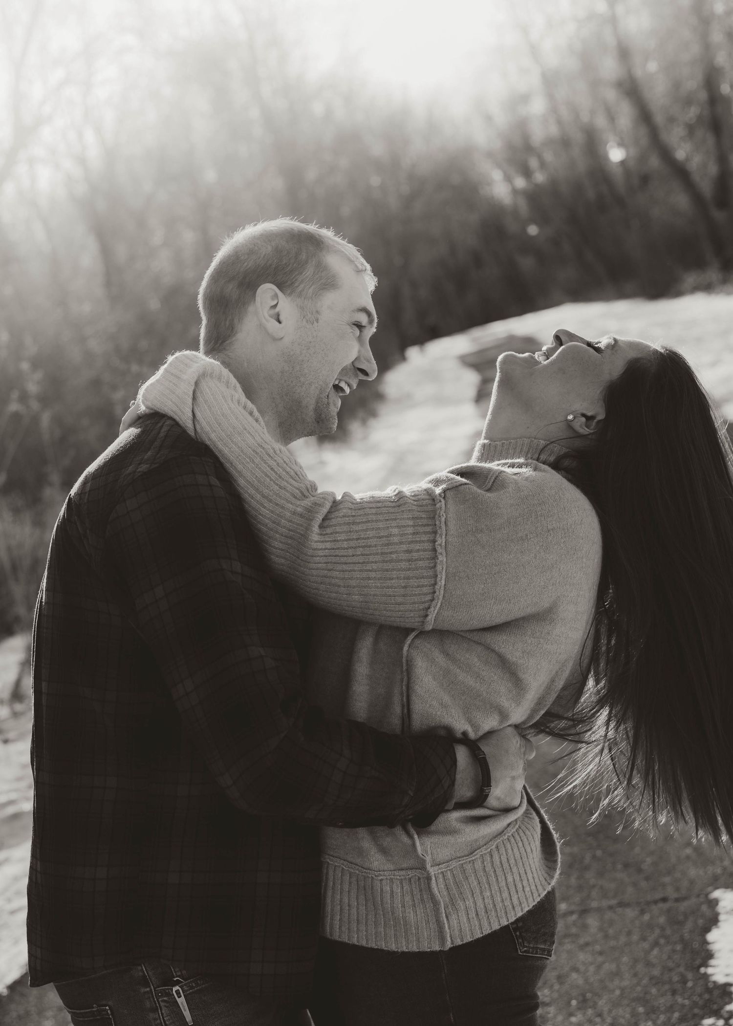 A romantic couple embraces and kisses in a dreamy outdoor setting with bare winter trees in the background.