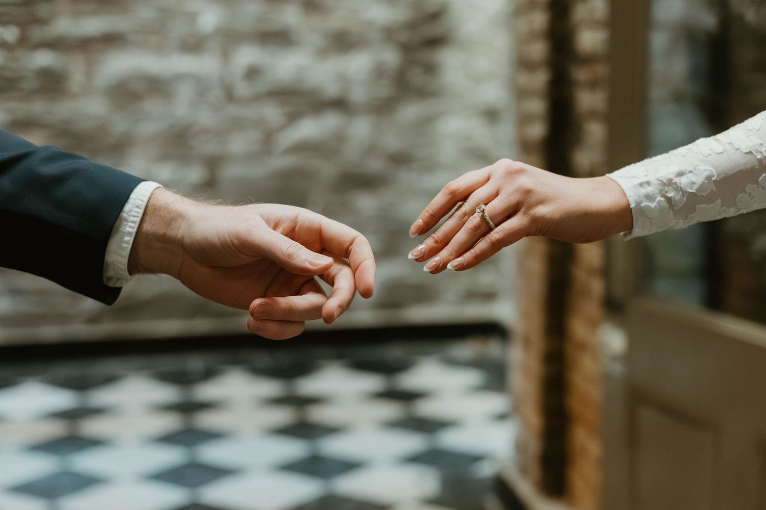 Two hands reaching out to exchange a wedding ring during an intimate ceremony on a checkered floor.